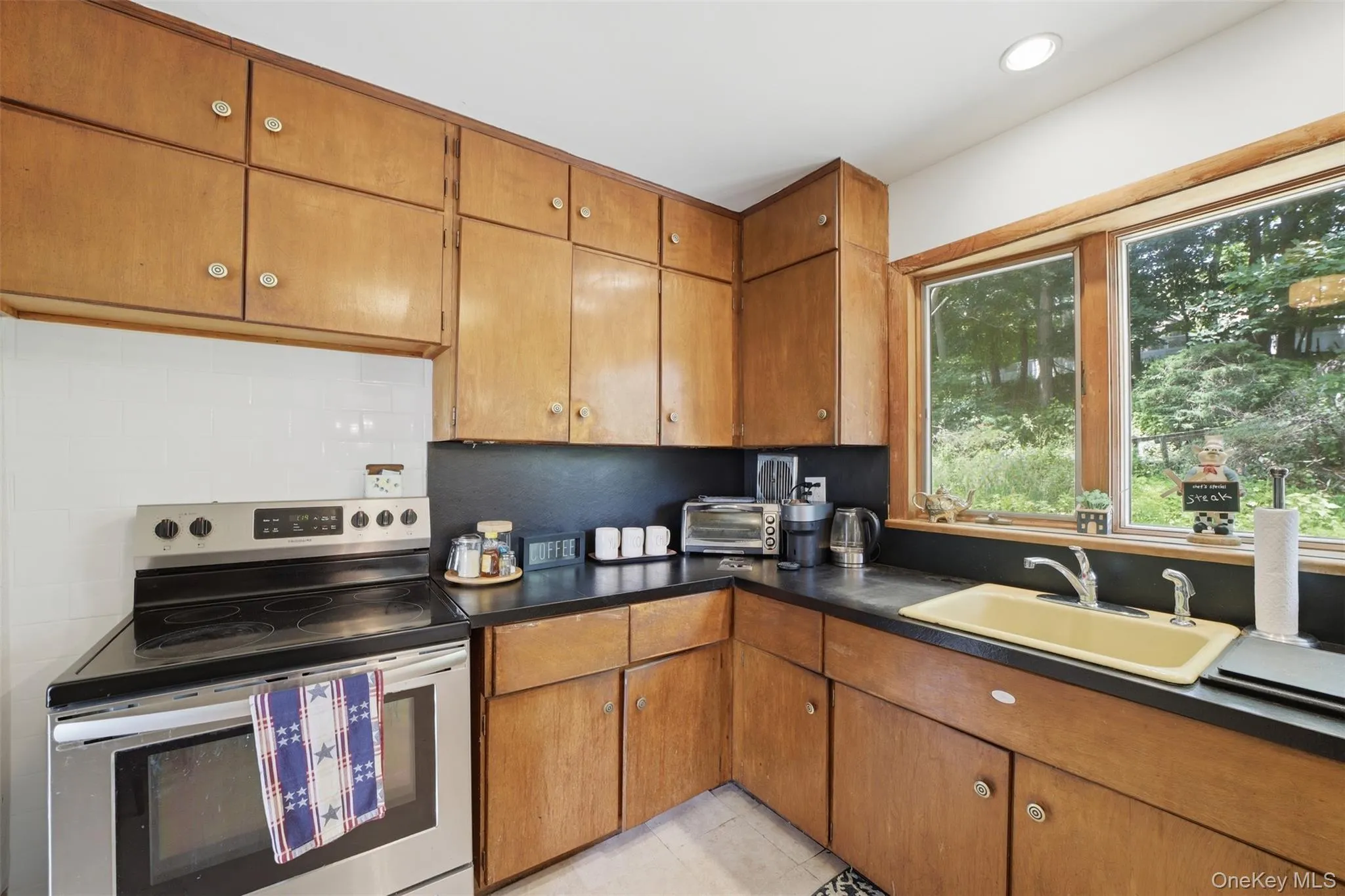 Kitchen featuring wood cabinetry, black countertops, and a white tiled backsplash Kitchen featuring wood cabinetry, black countertops, and a white tiled backsplash