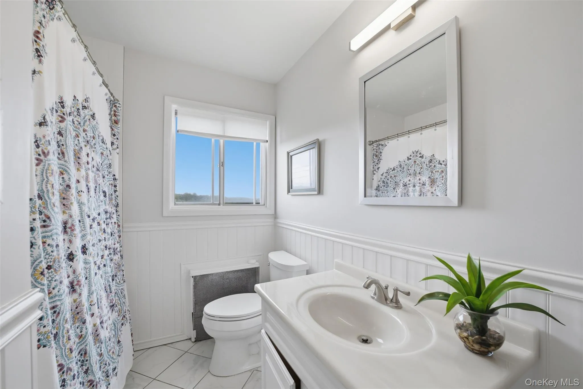 Full Hall Bathroom featuring white beadboard wainscoting, a window with natural light, a vanity with an integrated sink, a framed mirror, and tile flooring Full Hall Bathroom featuring white beadboard wainscoting, a window with natural light, a vanity with an integrated sink, a framed mirror, and tile flooring
