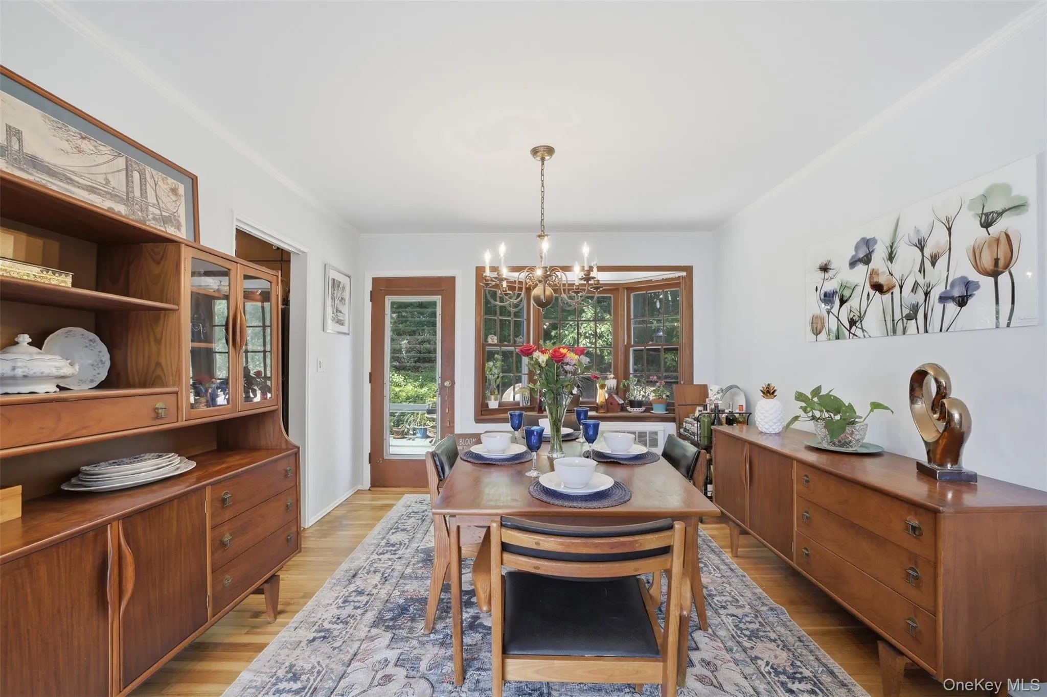 Dining area featuring wood-finish flooring, a brass chandelier, and a bay window with leaded glass details Dining area featuring wood-finish flooring, a brass chandelier, and a bay window with leaded glass details