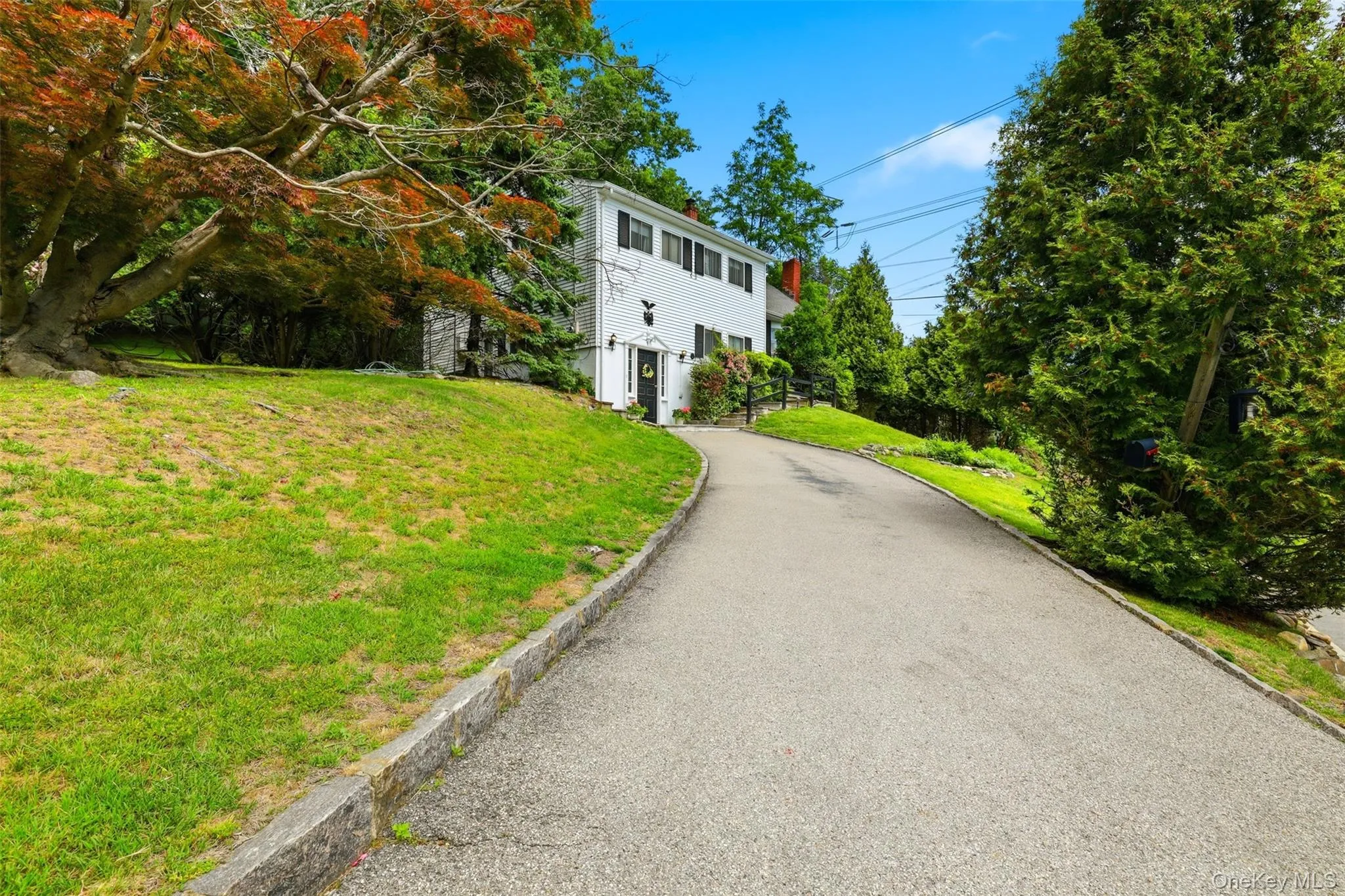 Paved driveway leading to a white two-story Colonial-style home with black shutters and a front entry porch Paved driveway leading to a white two-story Colonial-style home with black shutters and a front entry porch