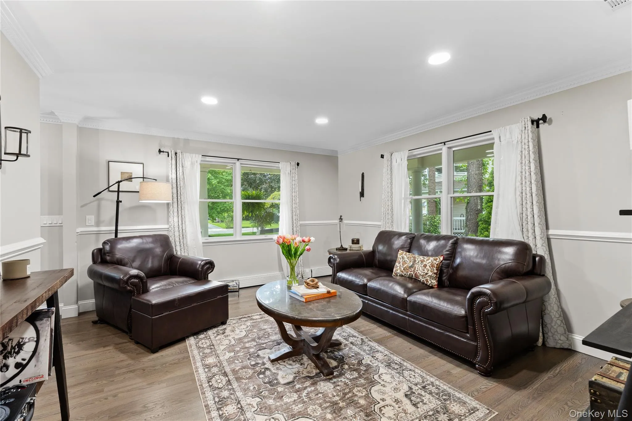 Spacious living area featuring wood-finish flooring, two large windows, recessed lighting, and crown molding Spacious living area featuring wood-finish flooring, two large windows, recessed lighting, and crown molding