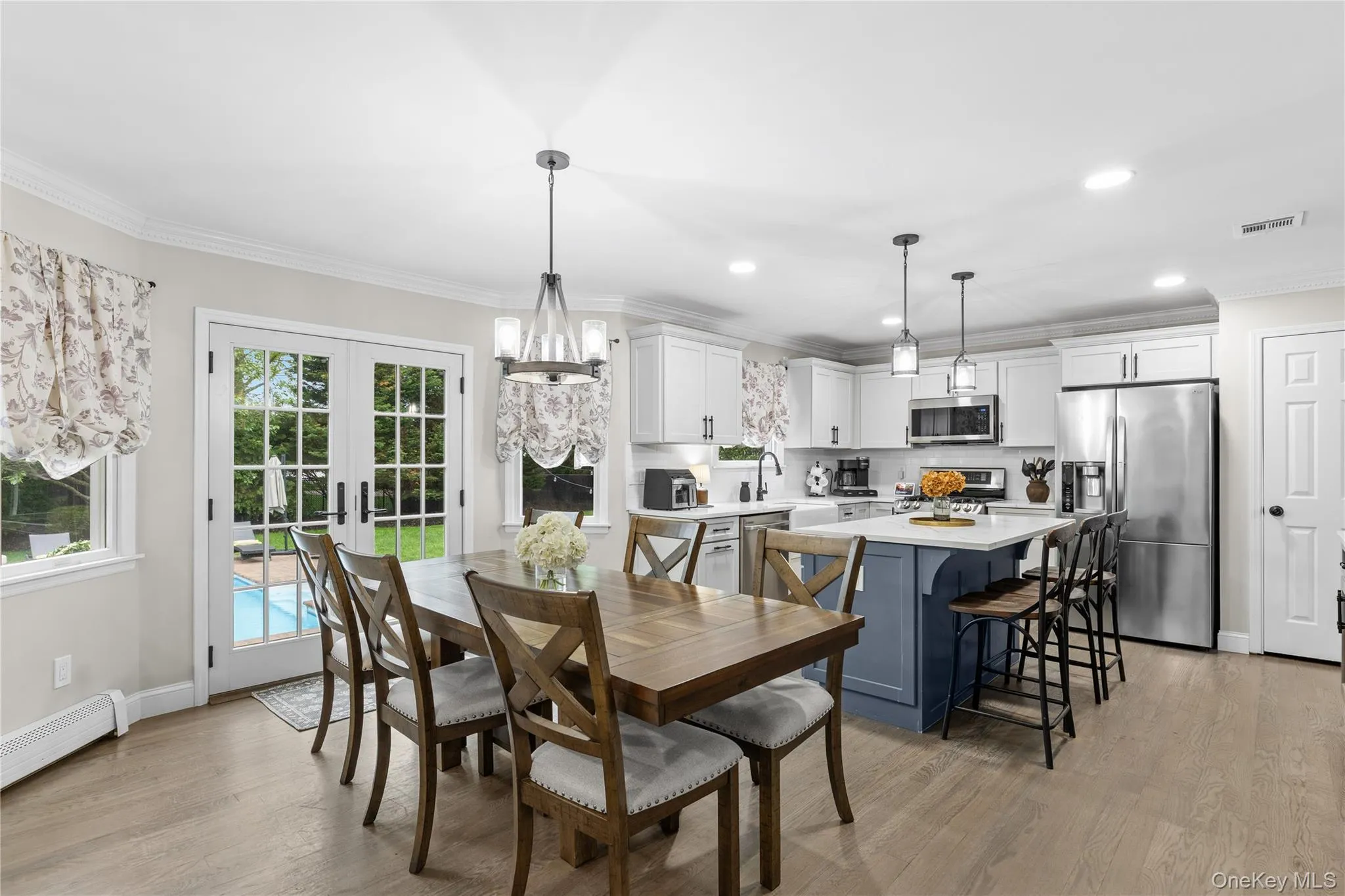 Open-concept kitchen and dining area featuring light wood-finish flooring, white cabinetry, stainless steel appliances, and a central island with a contrasting base Open-concept kitchen and dining area featuring light wood-finish flooring, white cabinetry, stainless steel appliances, and a central island with a contrasting base