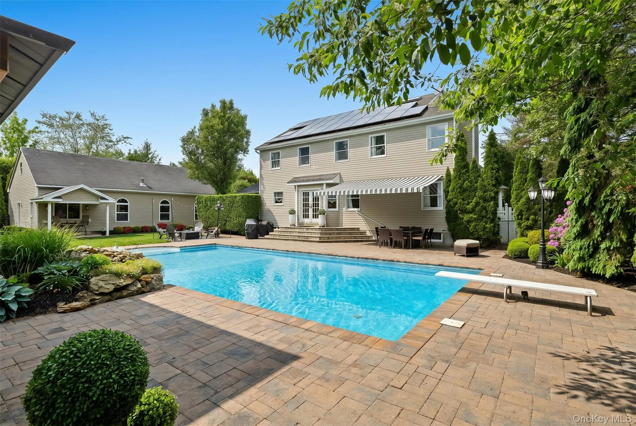 Expansive paver patio surrounding a salt water rectangular in-ground swimming pool with a diving board Expansive paver patio surrounding a salt water rectangular in-ground swimming pool with a diving board