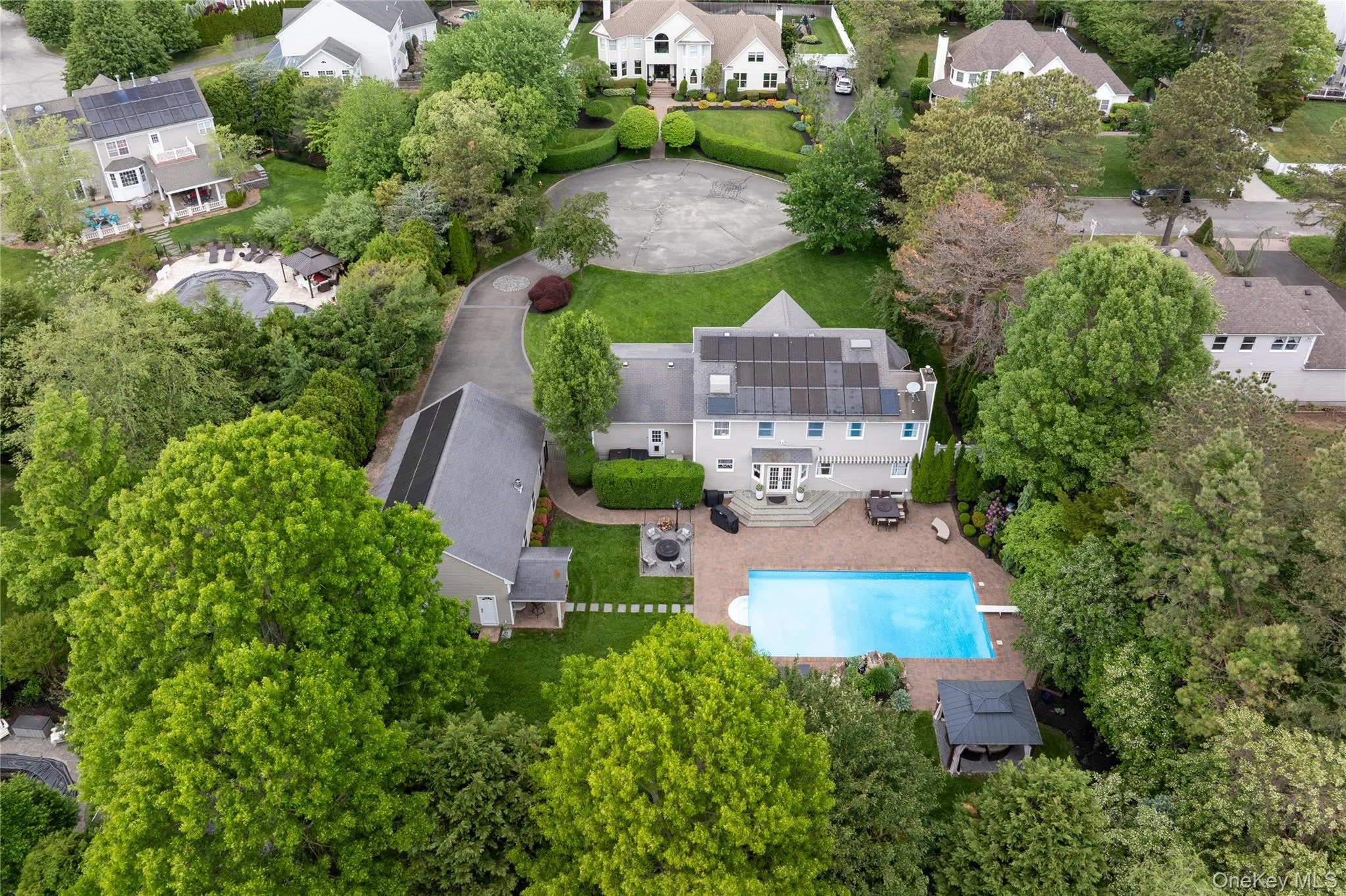 Expansive property featuring a large swimming pool, a substantial patio area, mature trees, a detached auxiliary structure, and multiple solar panel arrays Expansive property featuring a large swimming pool, a substantial patio area, mature trees, a detached auxiliary structure, and multiple solar panel arrays