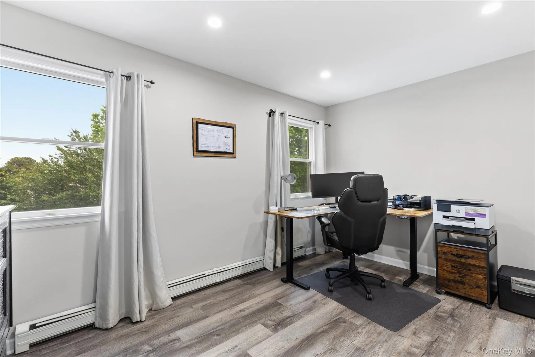 Room featuring wood-finish flooring, two windows with white trim, recessed lighting, and light gray wall paint Room featuring wood-finish flooring, two windows with white trim, recessed lighting, and light gray wall paint