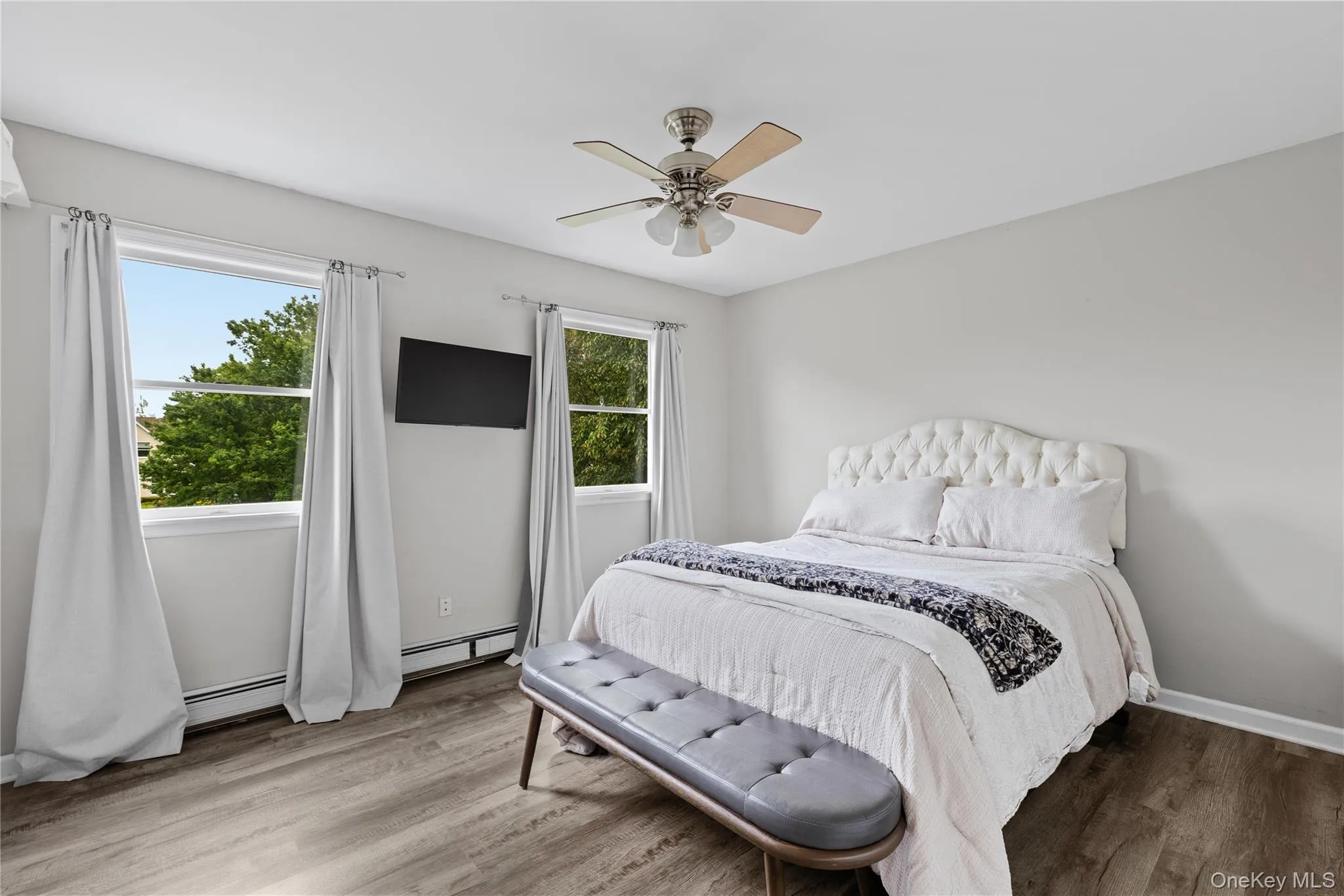 Bedroom featuring two windows, wood-finish flooring, a ceiling fan with integrated lighting, and light-colored walls Bedroom featuring two windows, wood-finish flooring, a ceiling fan with integrated lighting, and light-colored walls