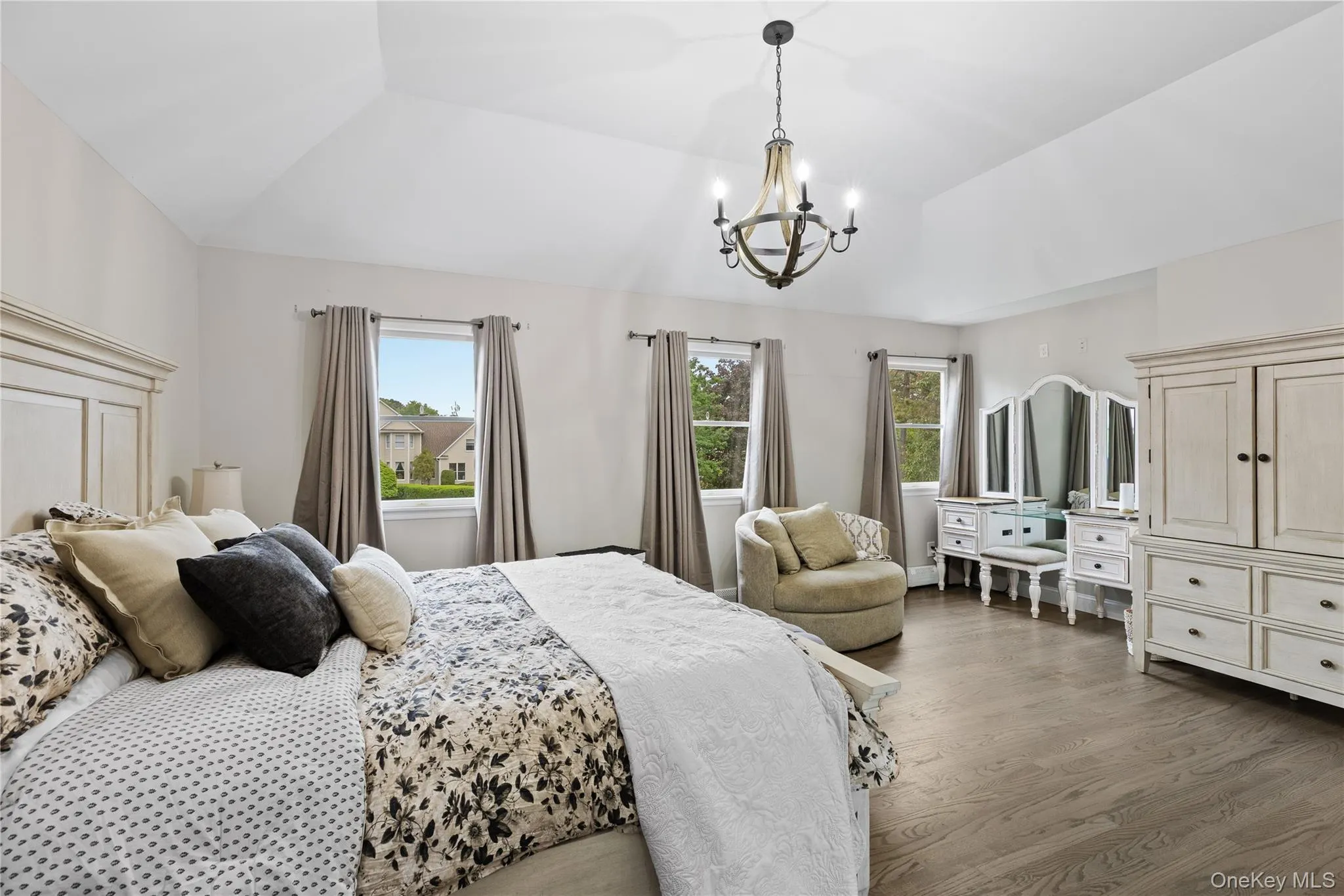 Vaulted ceiling bedroom featuring dark wood-finish flooring, a decorative chandelier, and abundant natural light from multiple windows Vaulted ceiling bedroom featuring dark wood-finish flooring, a decorative chandelier, and abundant natural light from multiple windows