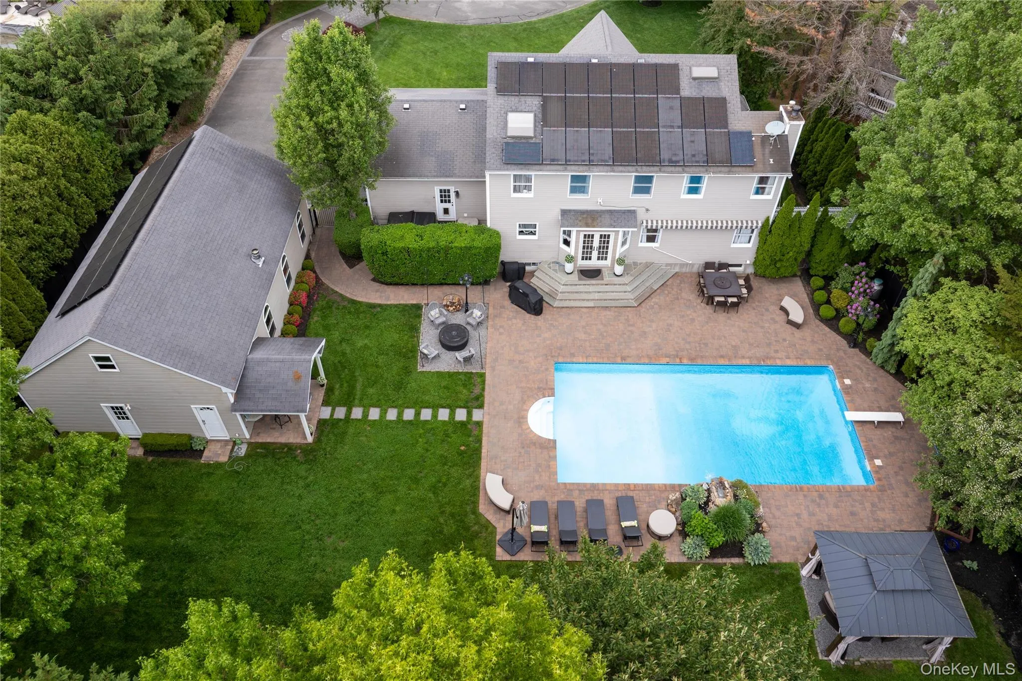 Expansive paver patio featuring an in-ground swimming pool, fire pit area, and a covered gazebo Expansive paver patio featuring an in-ground swimming pool, fire pit area, and a covered gazebo