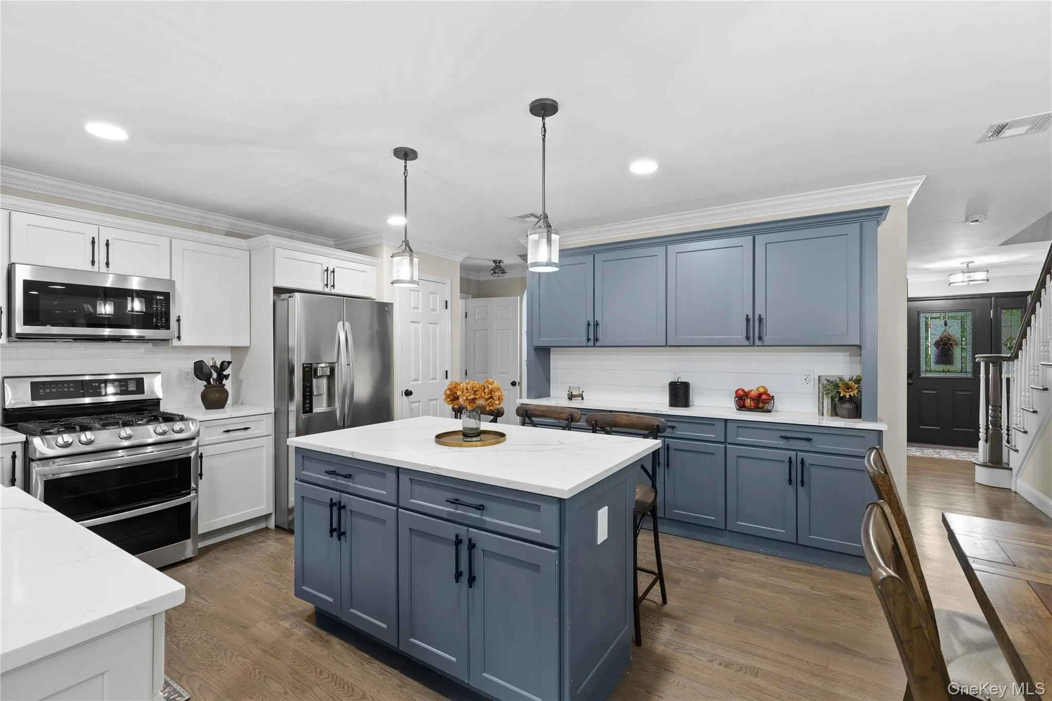 Gourmet kitchen with two-tone cabinetry, a central island, stainless steel appliances, quartz countertops, and wood-finish flooring Gourmet kitchen with two-tone cabinetry, a central island, stainless steel appliances, quartz countertops, and wood-finish flooring