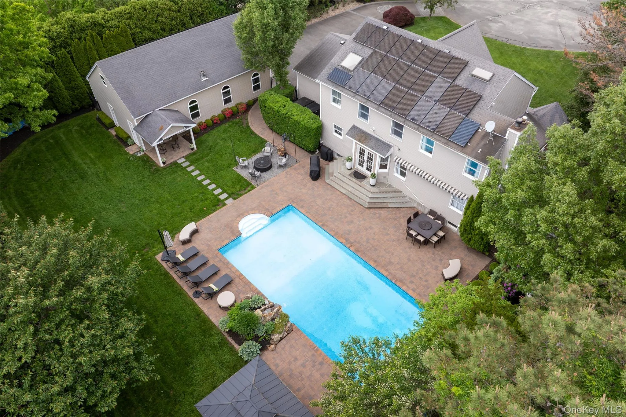 Expansive exterior featuring a rectangular swimming pool with brick paver surround, multiple outdoor seating areas, and a covered patio Expansive exterior featuring a rectangular swimming pool with brick paver surround, multiple outdoor seating areas, and a covered patio