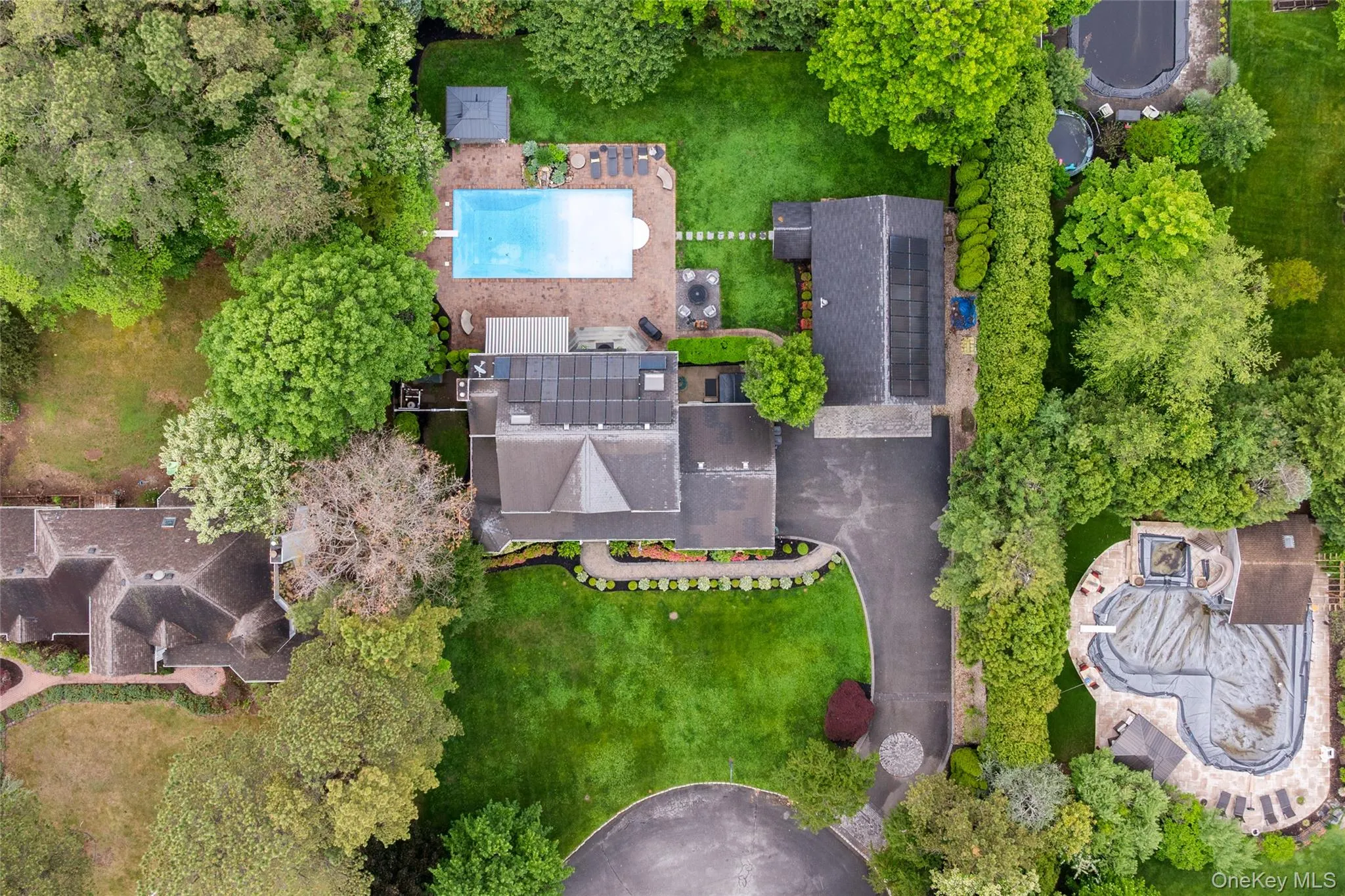 Expansive property featuring a rectangular swimming pool, mature perimeter landscaping, a paved driveway, and multiple structures with solar panels Expansive property featuring a rectangular swimming pool, mature perimeter landscaping, a paved driveway, and multiple structures with solar panels