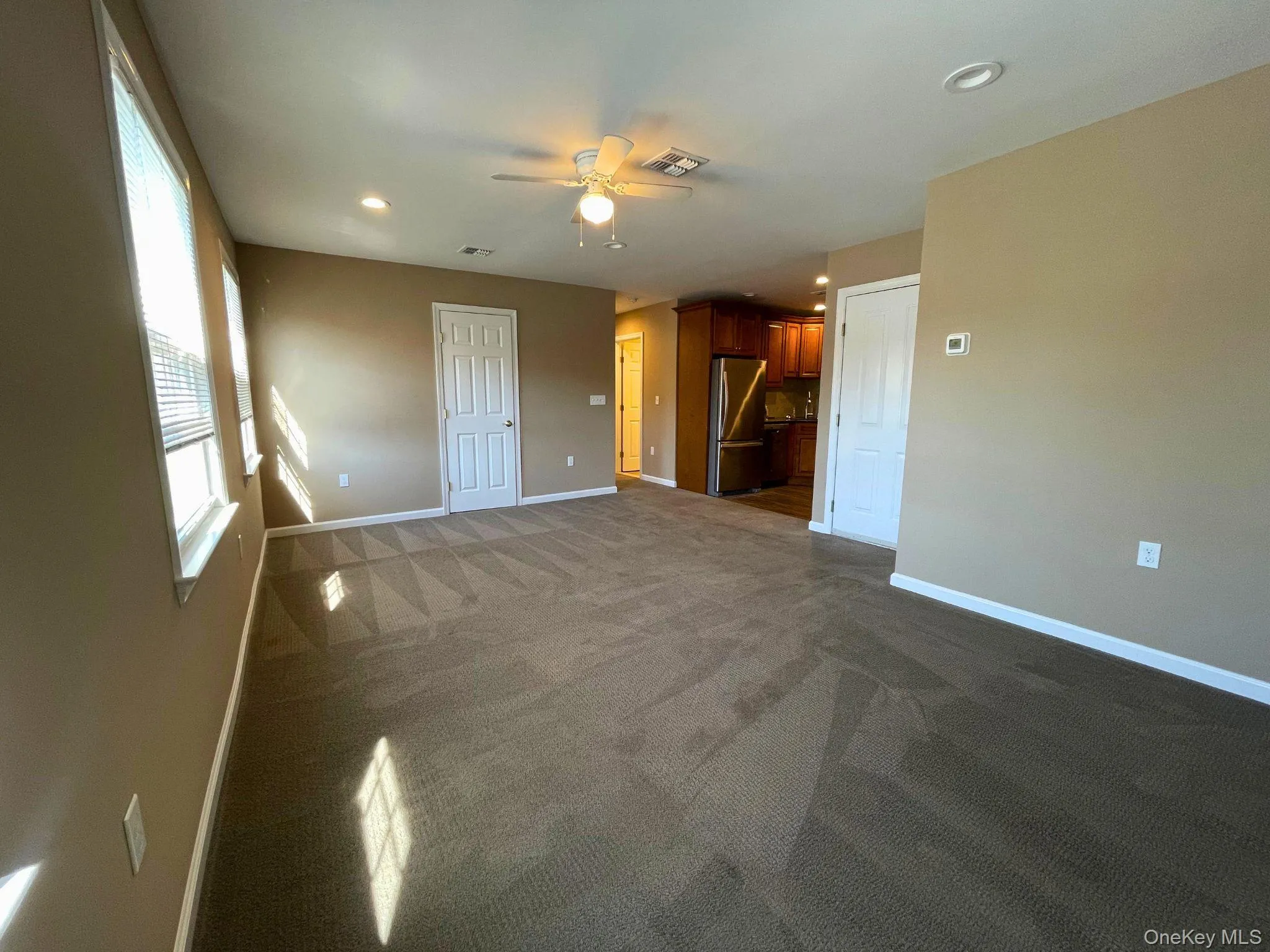 Spacious living area featuring neutral-toned walls and patterned carpeting Spacious living area featuring neutral-toned walls and patterned carpeting