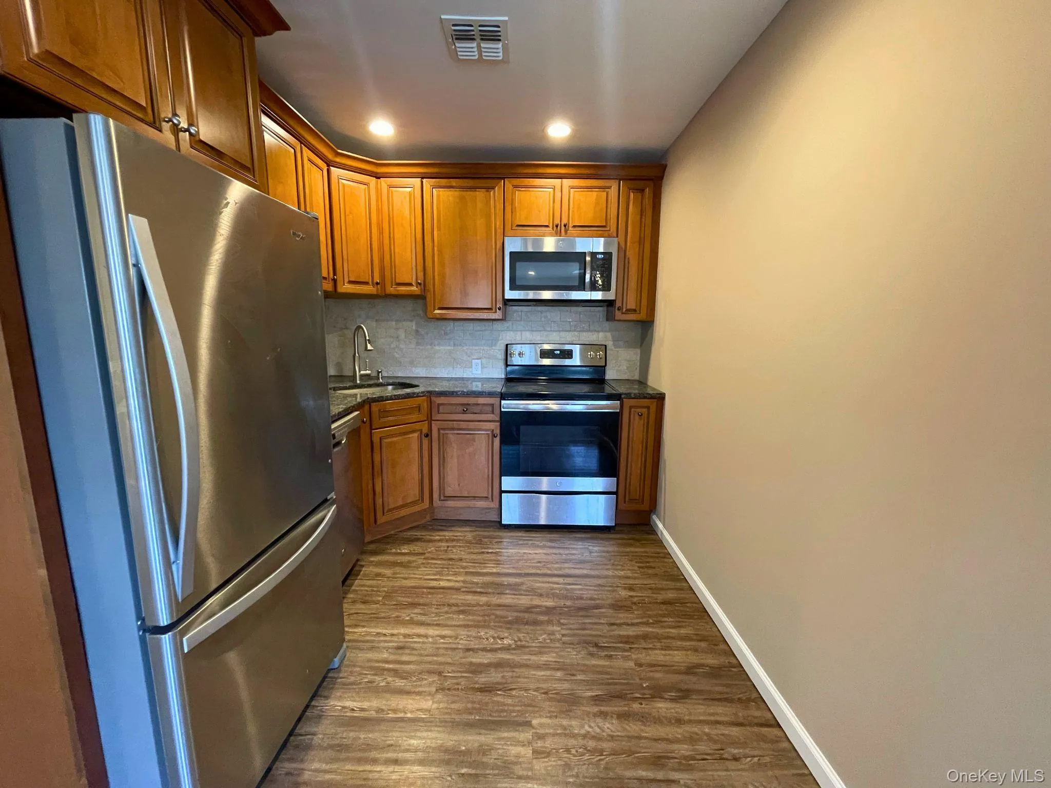 Kitchen featuring wood cabinetry, stainless steel appliances, dark countertops, and a tile backsplash Kitchen featuring wood cabinetry, stainless steel appliances, dark countertops, and a tile backsplash