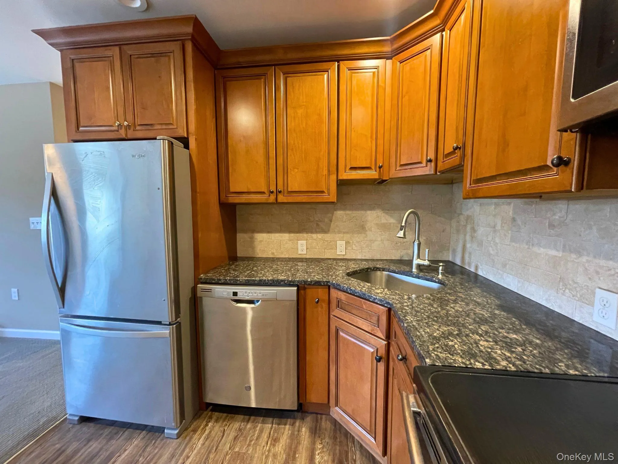 Kitchen featuring wood-finish cabinetry, stainless steel appliances, granite countertops, and stone tile backsplash Kitchen featuring wood-finish cabinetry, stainless steel appliances, granite countertops, and stone tile backsplash