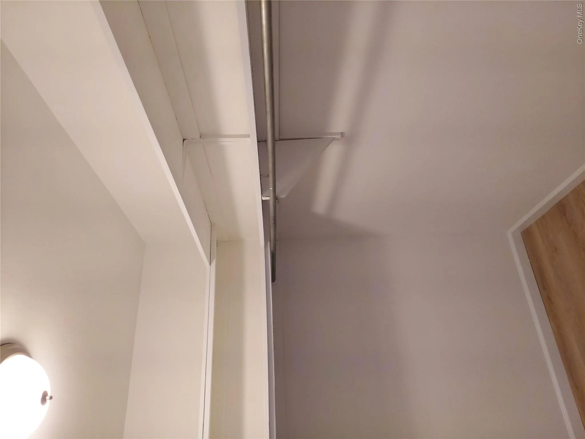 Interior closet featuring white walls, wood-finish flooring, a flush-mount ceiling light, and white built-in shelving with hanging rods Interior closet featuring white walls, wood-finish flooring, a flush-mount ceiling light, and white built-in shelving with hanging rods