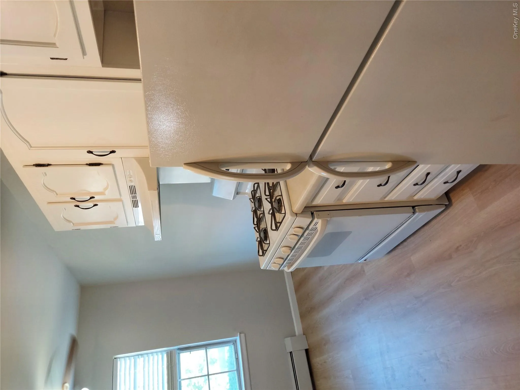 Kitchen area featuring light wood-finish flooring, white cabinetry with black hardware, a white gas range, and a white refrigerator Kitchen area featuring light wood-finish flooring, white cabinetry with black hardware, a white gas range, and a white refrigerator