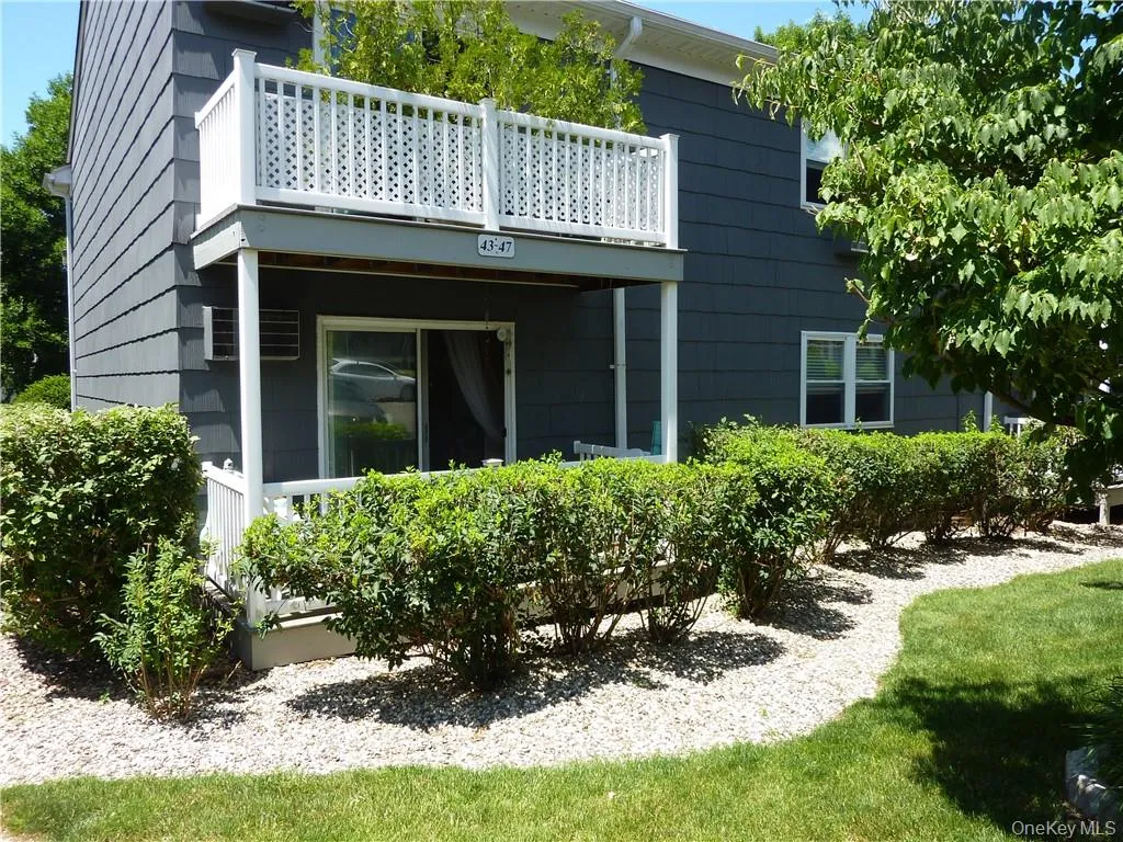 Exterior featuring charcoal gray siding, a white lattice balcony railing, and a ground-level patio with white railings Exterior featuring charcoal gray siding, a white lattice balcony railing, and a ground-level patio with white railings