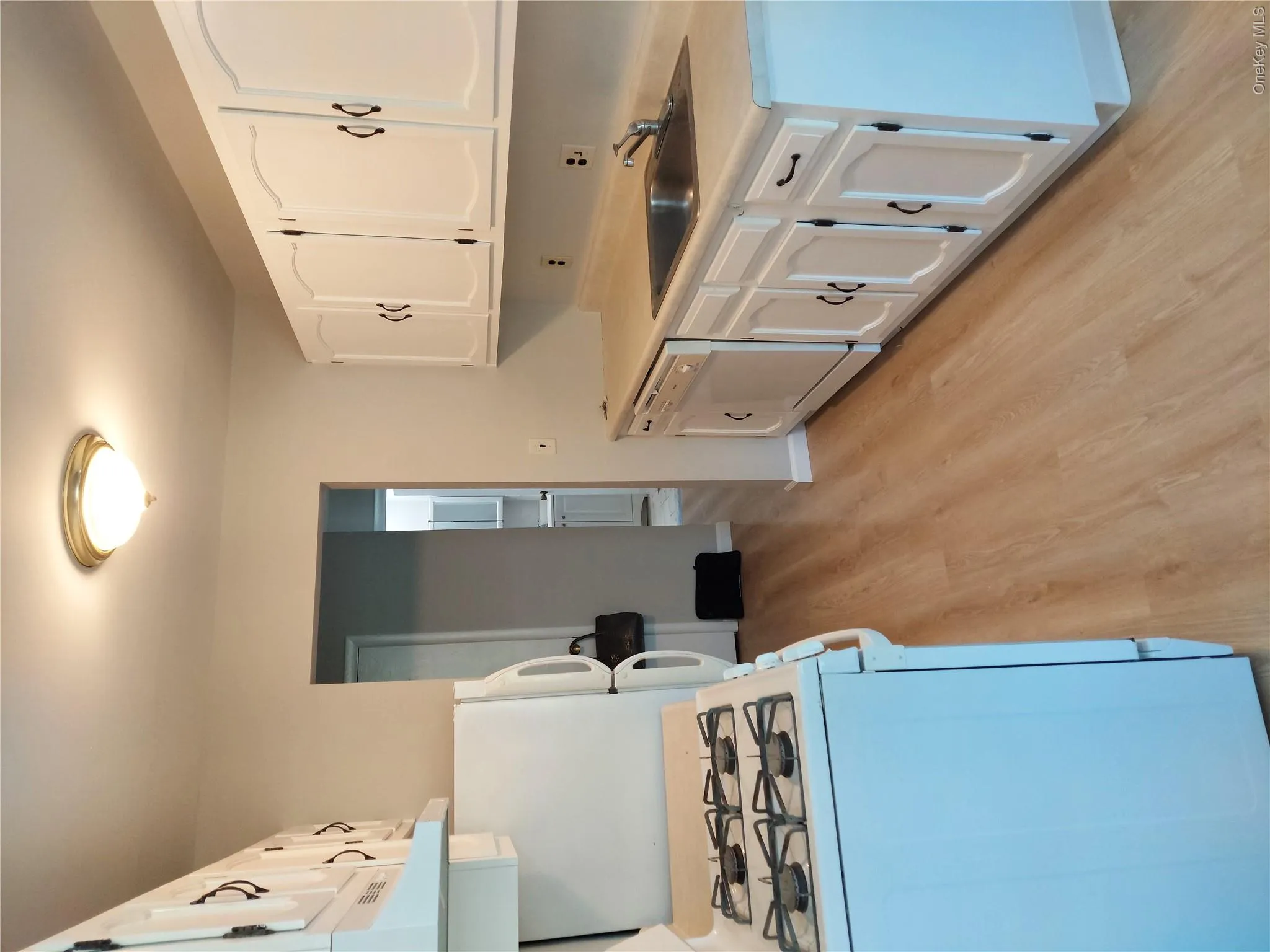 Kitchen featuring white cabinetry with dark hardware, a white gas range, white refrigerator, white dishwasher, and light wood-finish flooring Kitchen featuring white cabinetry with dark hardware, a white gas range, white refrigerator, white dishwasher, and light wood-finish flooring