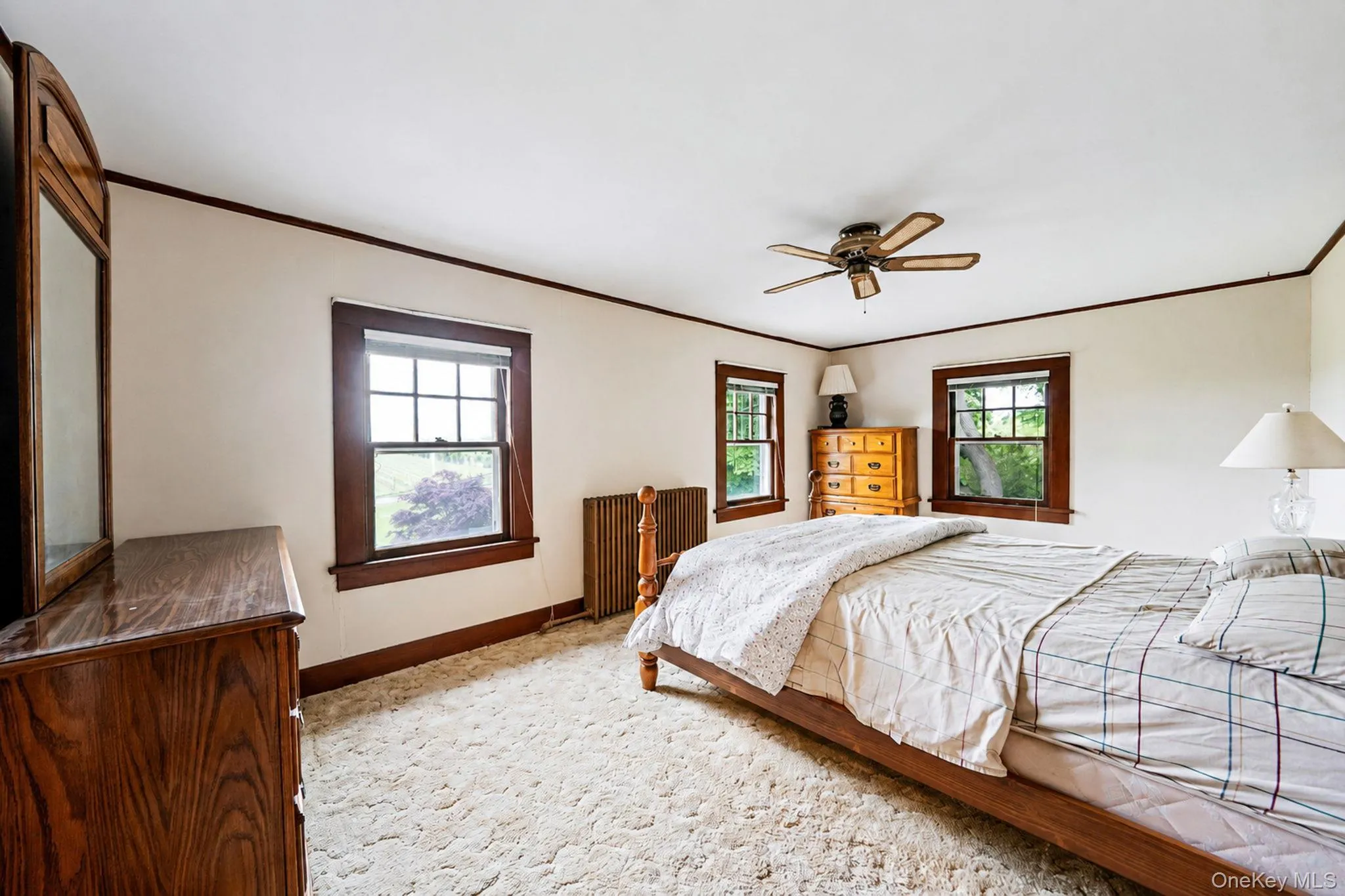 Spacious room featuring multiple windows with wood trim, ceiling fan, and light-colored carpeting. Wood floors under the carpeting. Spacious room featuring multiple windows with wood trim, ceiling fan, and light-colored carpeting. Wood floors under the carpeting.