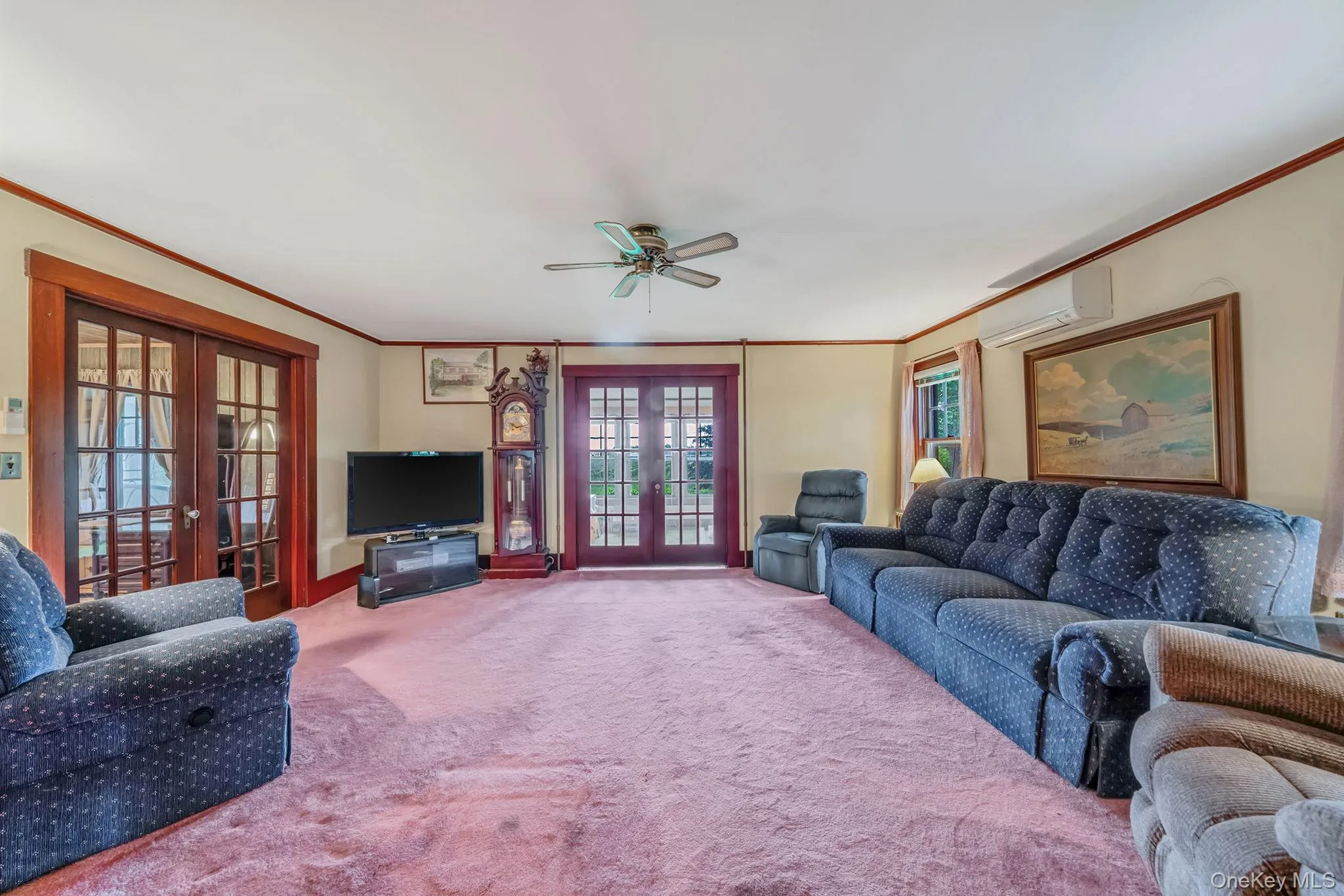 Spacious living area featuring two sets of French doors to Den/Bedroom/Office, an overhead ceiling fan, and light-colored walls with wood trim Spacious living area featuring two sets of French doors to Den/Bedroom/Office, an overhead ceiling fan, and light-colored walls with wood trim