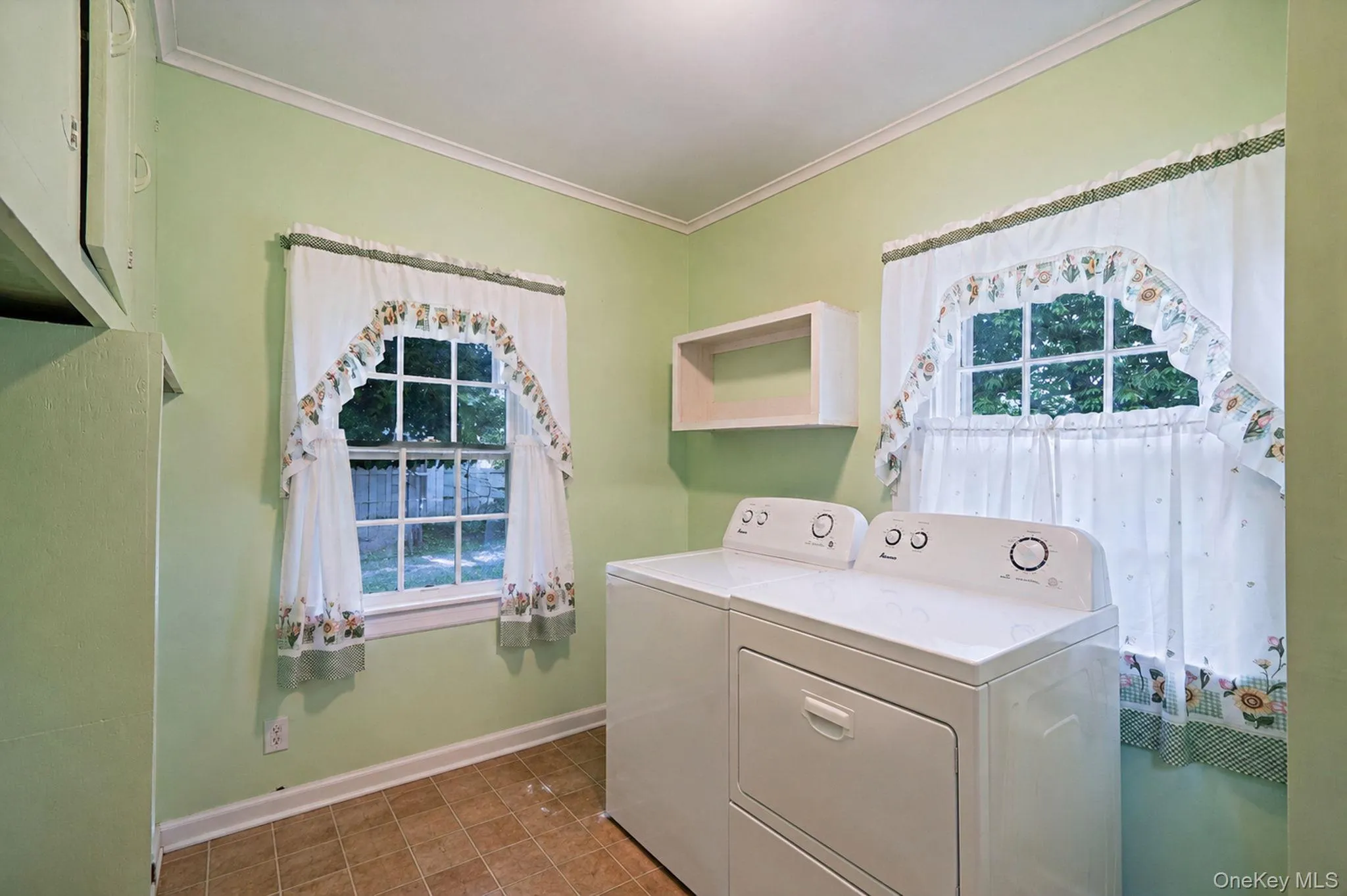 Laundry room featuring dual windows, crown molding, a built-in wall cabinet, and durable tile-finish flooring Laundry room featuring dual windows, crown molding, a built-in wall cabinet, and durable tile-finish flooring
