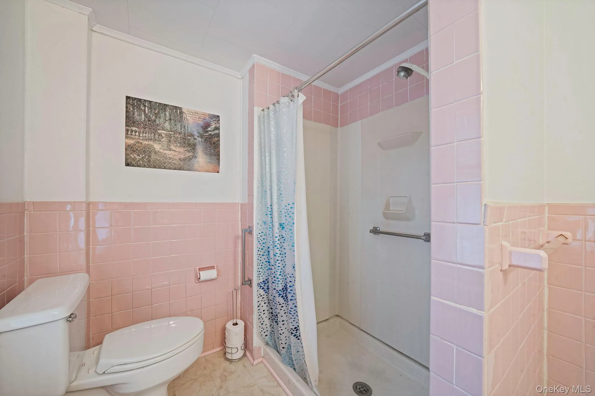 Bathroom featuring full pink wall tiling, a white toilet, and a stand-up shower with a grab bar Bathroom featuring full pink wall tiling, a white toilet, and a stand-up shower with a grab bar