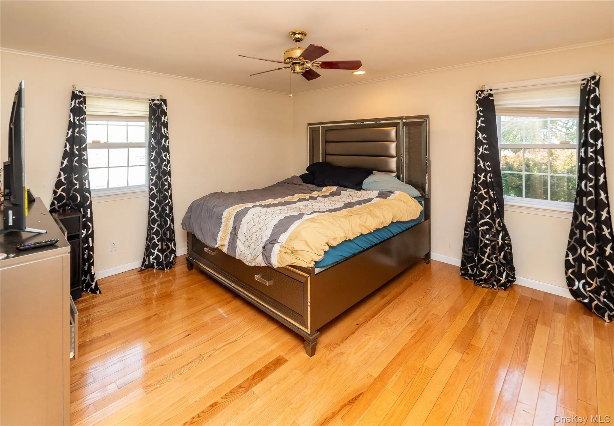 Spacious room featuring wood-finish flooring, two windows with white trim, and a ceiling fan with integrated lighting Spacious room featuring wood-finish flooring, two windows with white trim, and a ceiling fan with integrated lighting