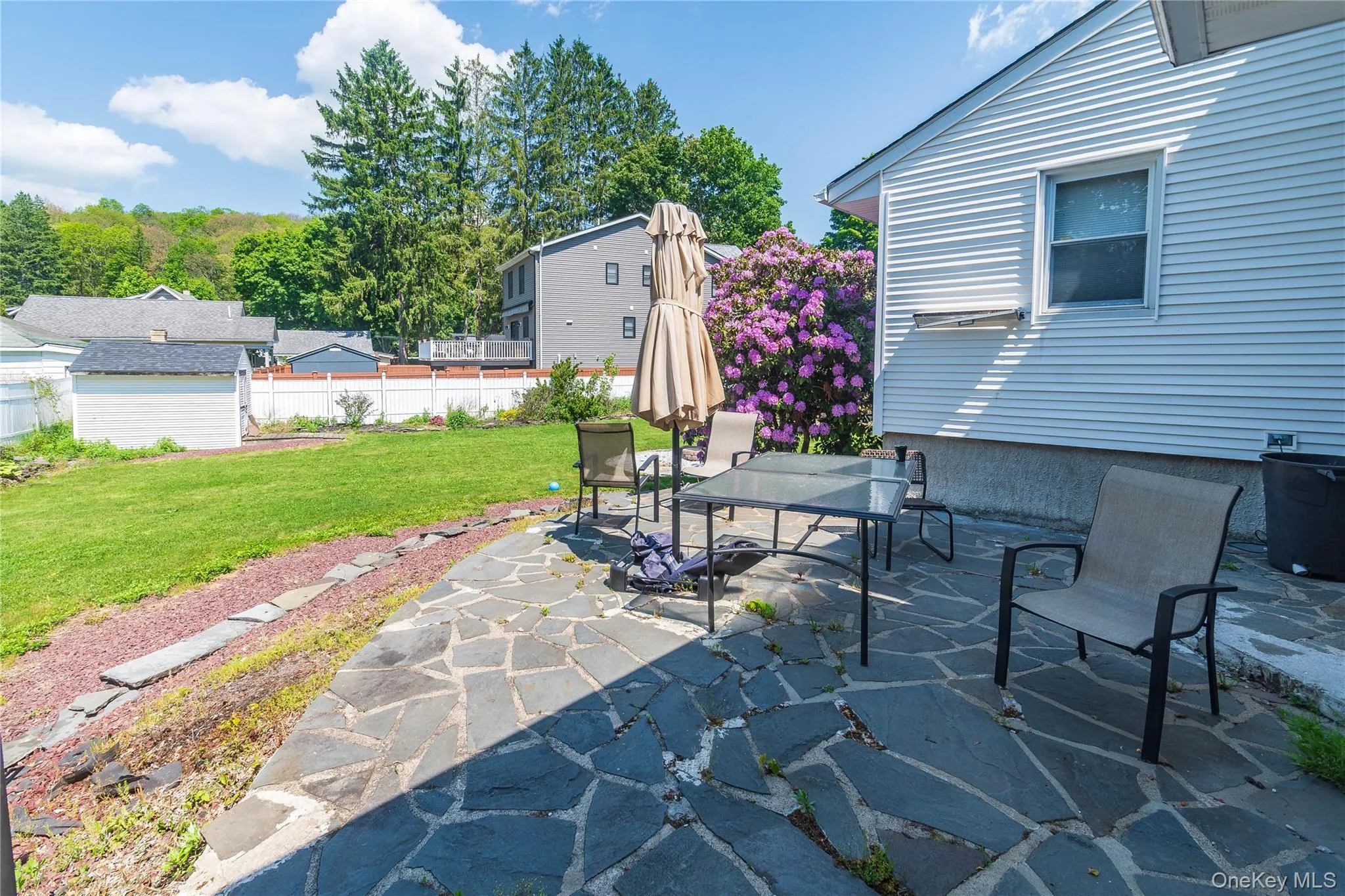 Spacious backyard featuring a flagstone patio, manicured lawn, and white privacy fencing Spacious backyard featuring a flagstone patio, manicured lawn, and white privacy fencing