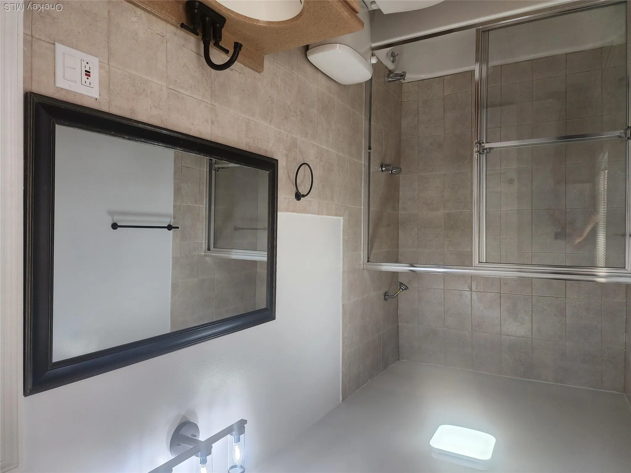 Bathroom featuring a tiled tub-shower combination with sliding glass doors, a vanity with an undermount sink, a framed mirror, and modern lighting fixtures and tiled floor Bathroom featuring a tiled tub-shower combination with sliding glass doors, a vanity with an undermount sink, a framed mirror, and modern lighting fixtures and tiled floor