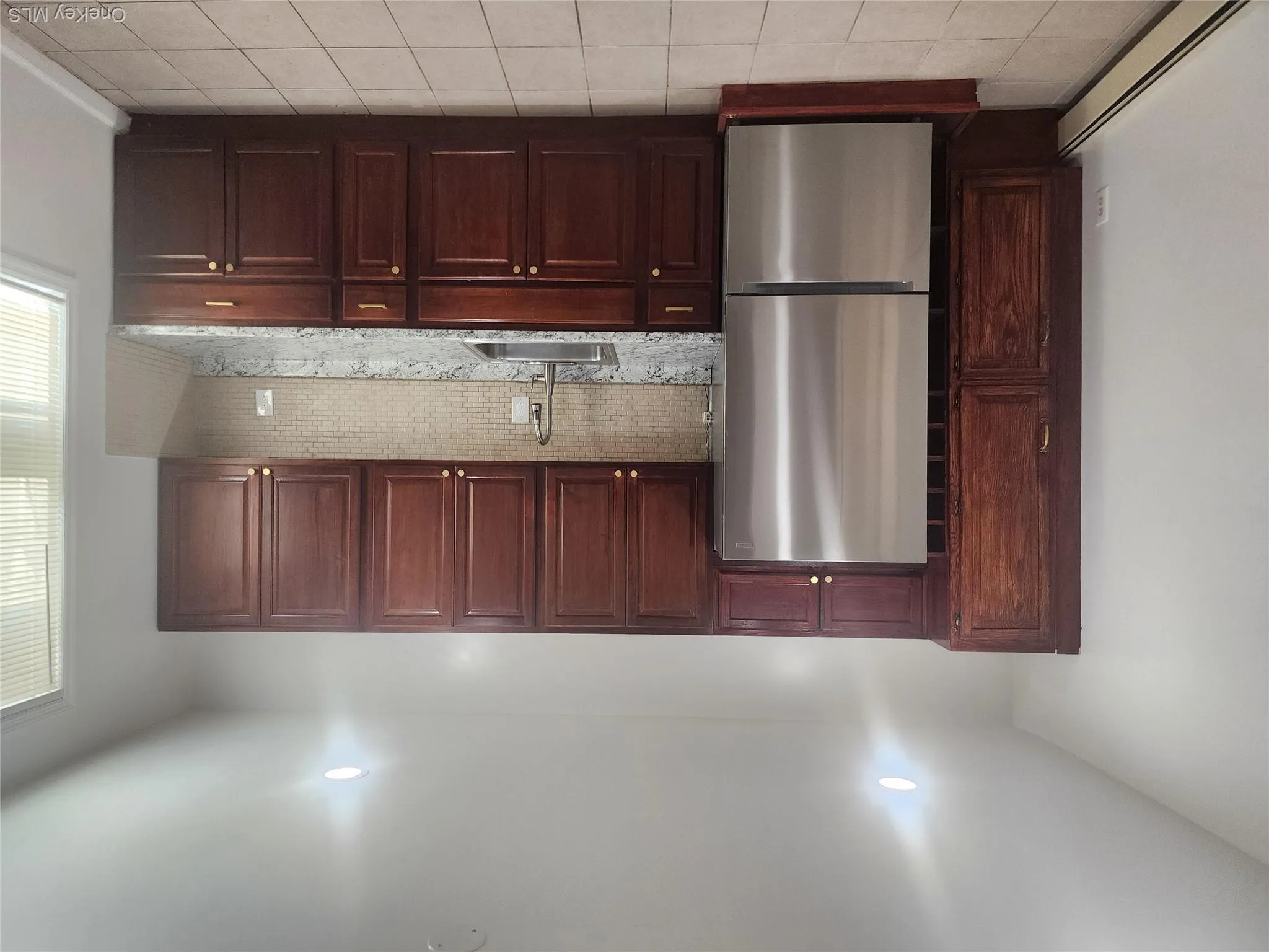 Kitchen featuring wood cabinetry, stainless steel refrigerator, stone-finish countertops, and a tiled backsplash Kitchen featuring wood cabinetry, stainless steel refrigerator, stone-finish countertops, and a tiled backsplash