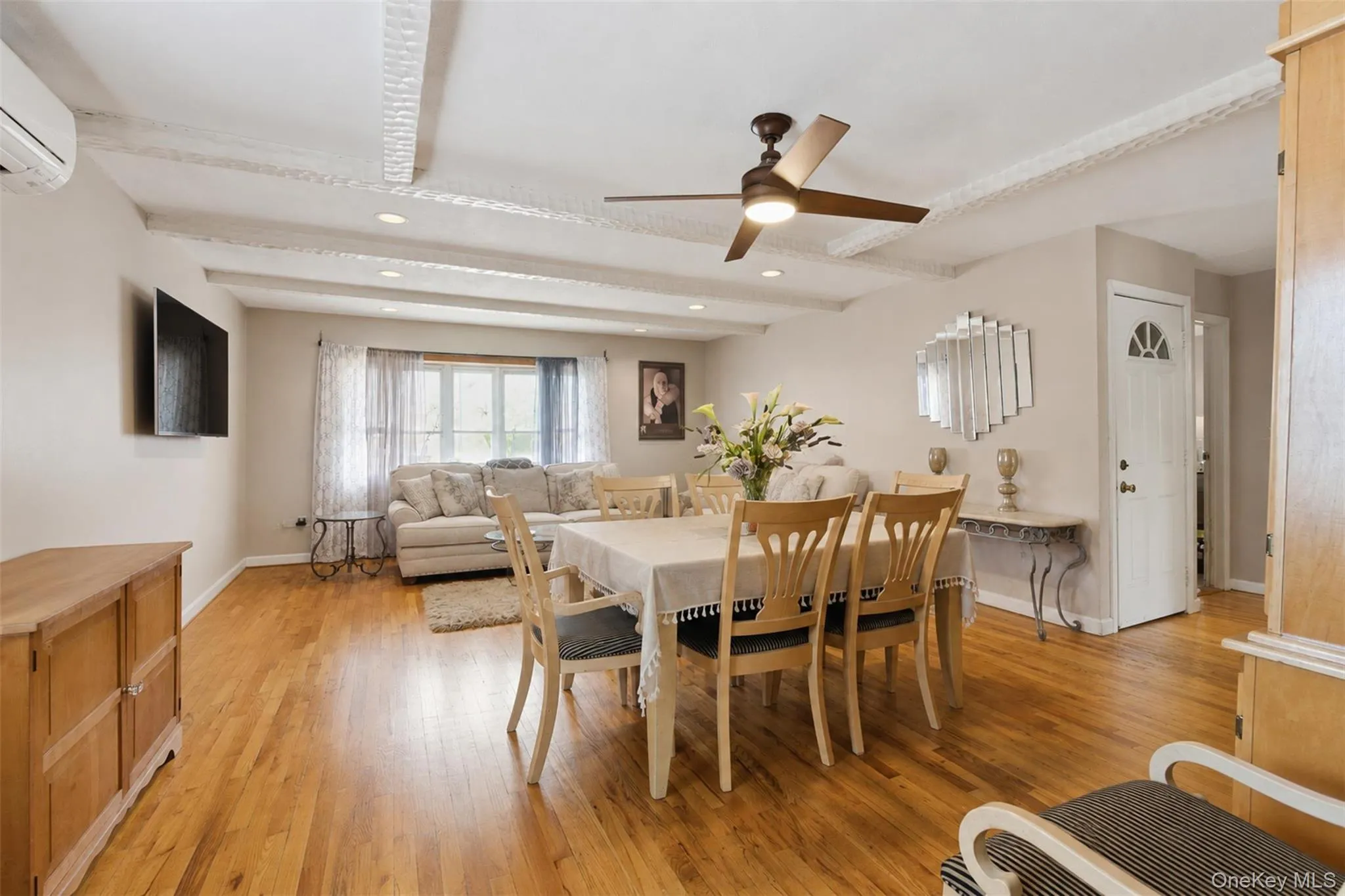 Open-concept living and dining area featuring wood-finish flooring, exposed beam ceiling detailing, and recessed lighting Open-concept living and dining area featuring wood-finish flooring, exposed beam ceiling detailing, and recessed lighting