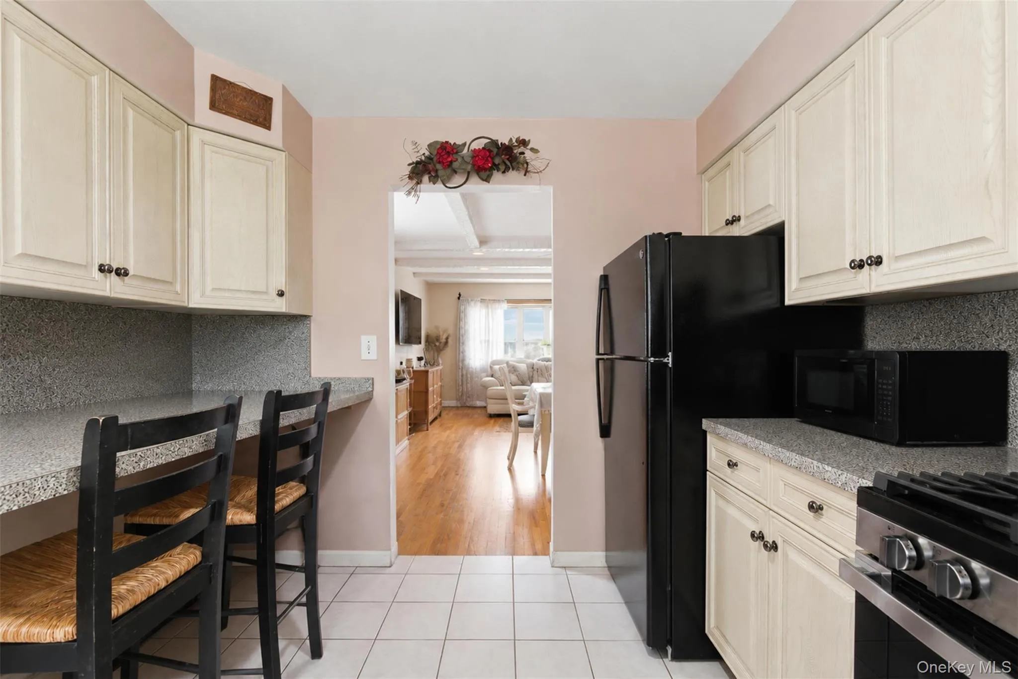 Kitchen featuring white shaker-style cabinetry, a built-in counter bar, a black refrigerator, a stainless steel range, and tile flooring Kitchen featuring white shaker-style cabinetry, a built-in counter bar, a black refrigerator, a stainless steel range, and tile flooring