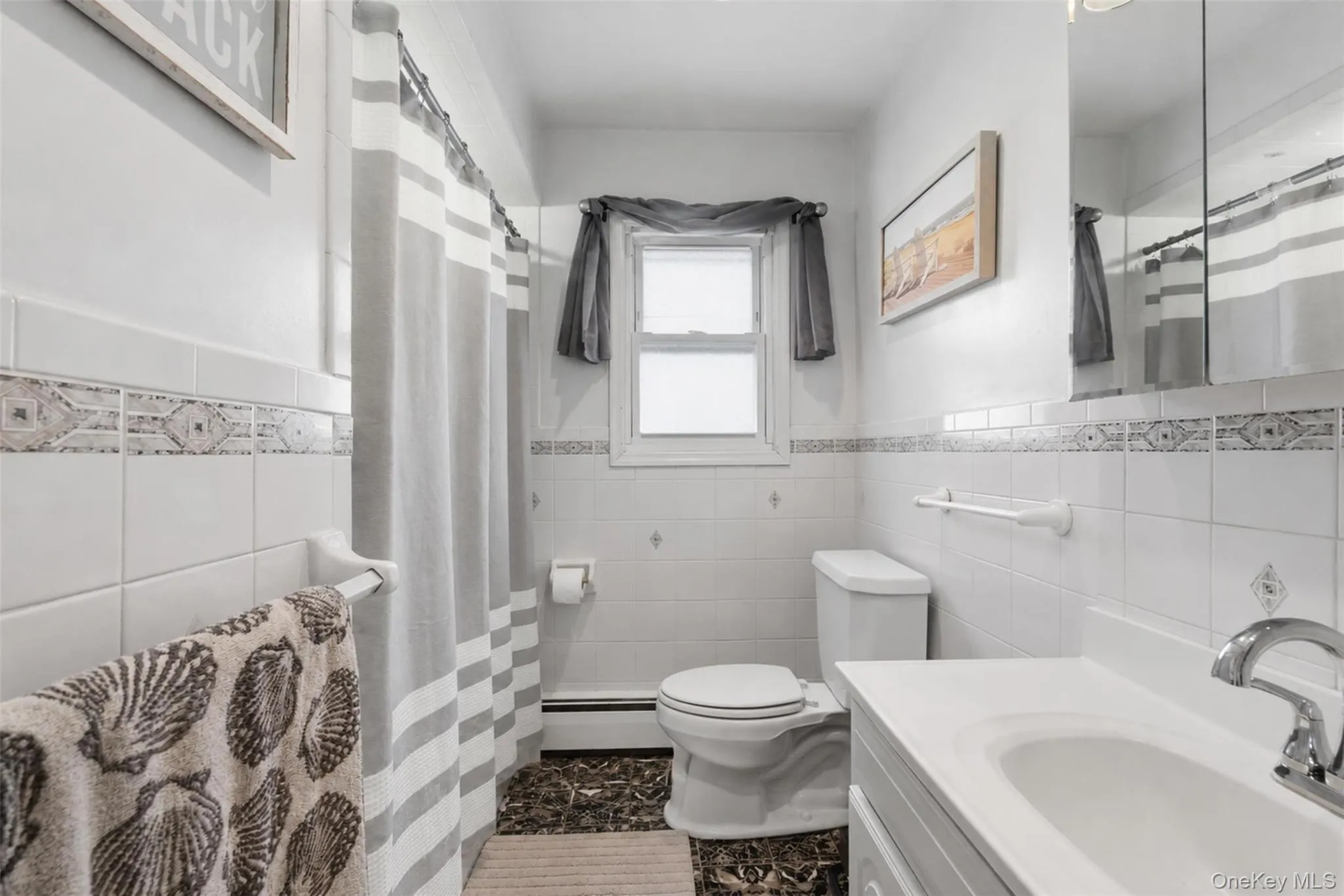 Bathroom featuring white ceramic wall tiling, an ornamental tile border, a built-in vanity with an integrated sink, a built-in medicine cabinet, and a window for natural light Bathroom featuring white ceramic wall tiling, an ornamental tile border, a built-in vanity with an integrated sink, a built-in medicine cabinet, and a window for natural light