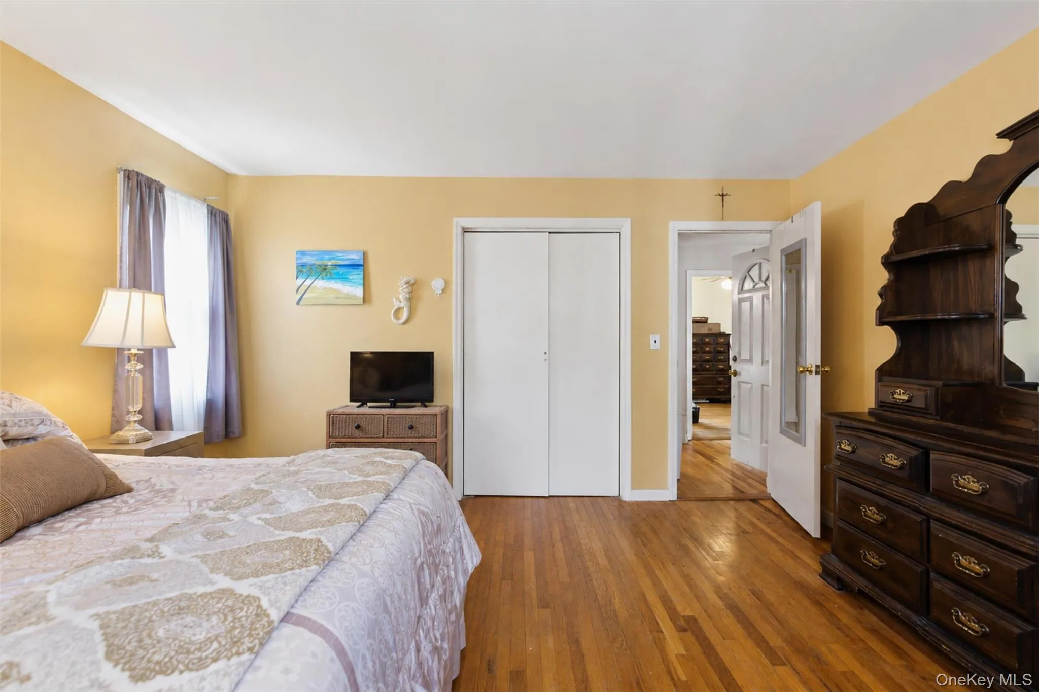Hardwood flooring throughout, featuring a window with natural light, a closet with bi-fold doors, and a paneled interior door Hardwood flooring throughout, featuring a window with natural light, a closet with bi-fold doors, and a paneled interior door