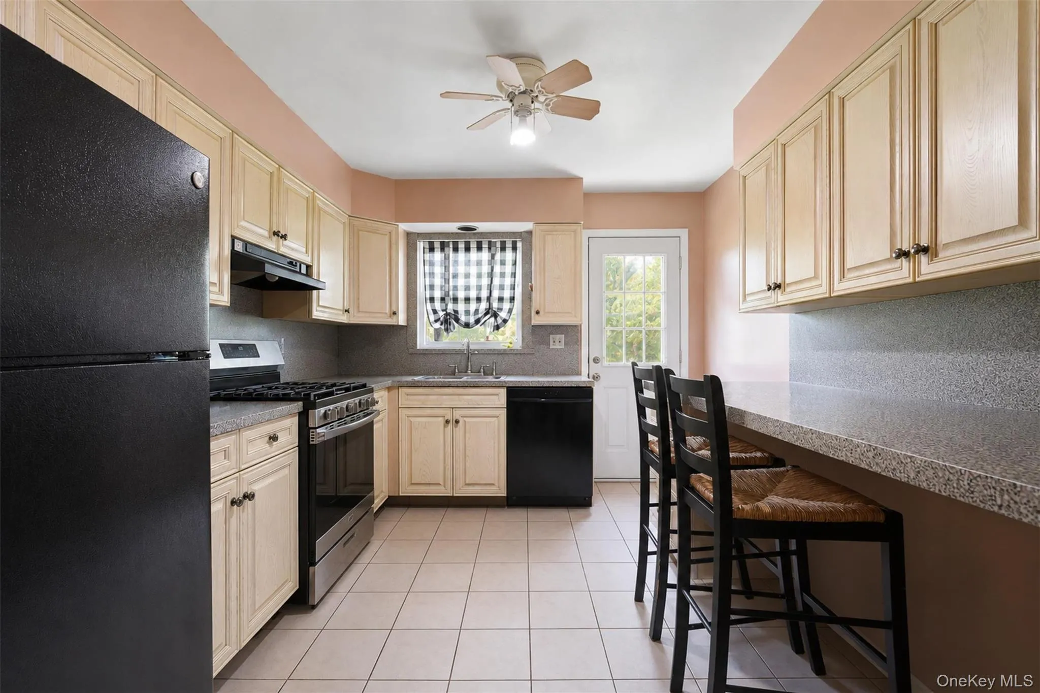 Kitchen featuring light-toned cabinetry, a built-in breakfast bar with seating, a window above the sink, a ceiling fan, and tile flooring Kitchen featuring light-toned cabinetry, a built-in breakfast bar with seating, a window above the sink, a ceiling fan, and tile flooring