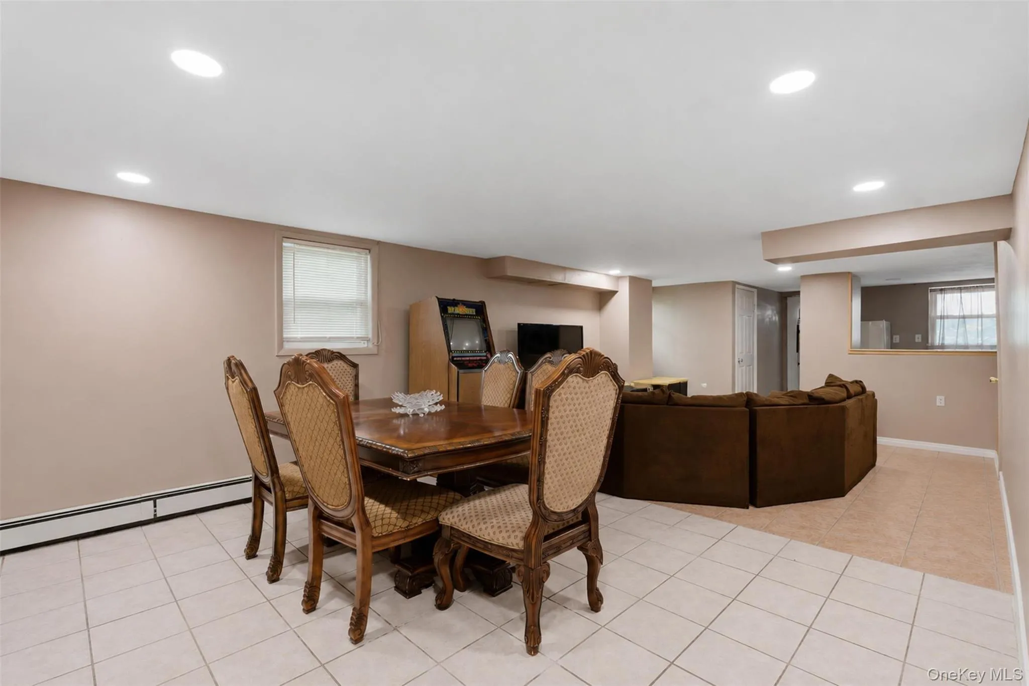 Expansive finished room featuring recessed lighting, a window with blinds, and light-toned tile flooring throughout the foreground Expansive finished room featuring recessed lighting, a window with blinds, and light-toned tile flooring throughout the foreground