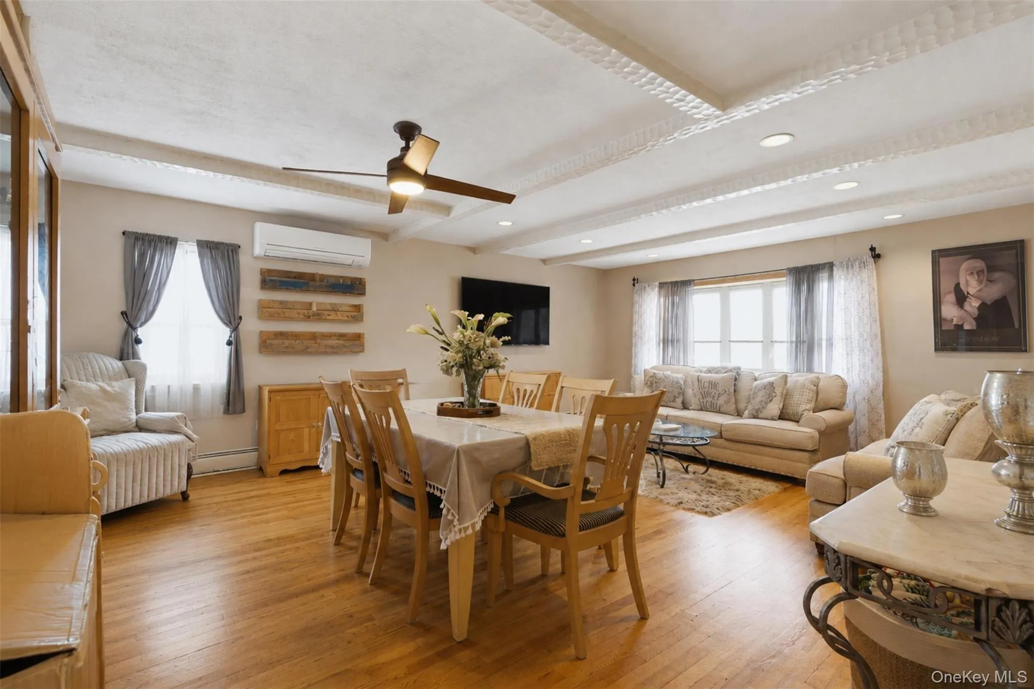 Spacious main living area featuring wood-finish flooring, a decorative tray ceiling with recessed lighting, and a ceiling fan Spacious main living area featuring wood-finish flooring, a decorative tray ceiling with recessed lighting, and a ceiling fan