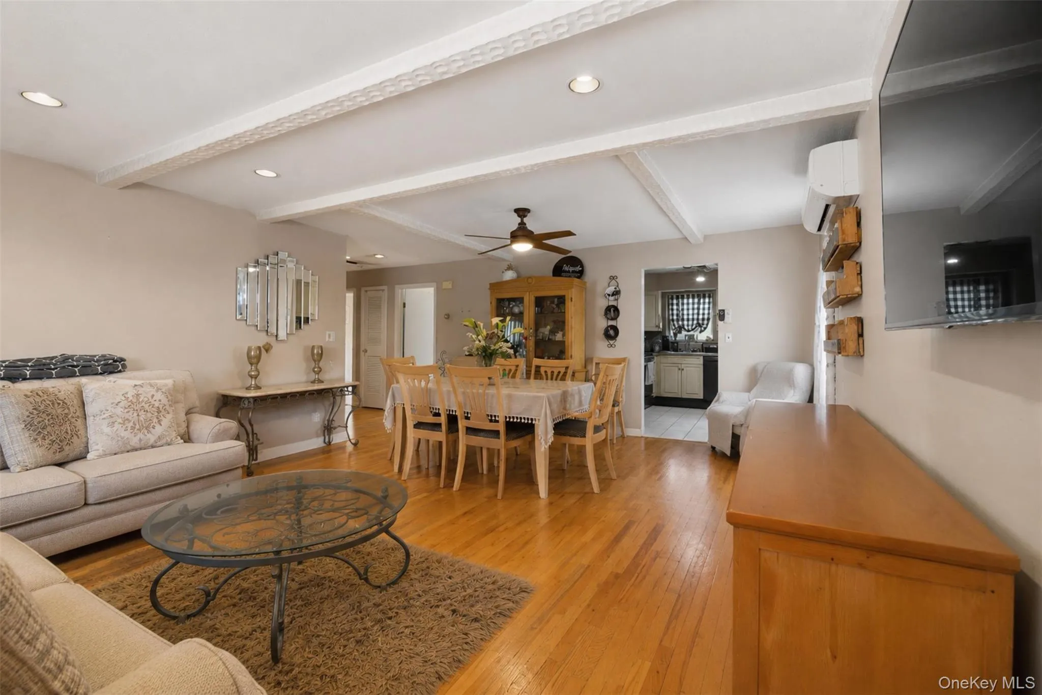 Open concept living and dining area featuring wood-finish flooring, recessed lighting, and decorative ceiling beams Open concept living and dining area featuring wood-finish flooring, recessed lighting, and decorative ceiling beams