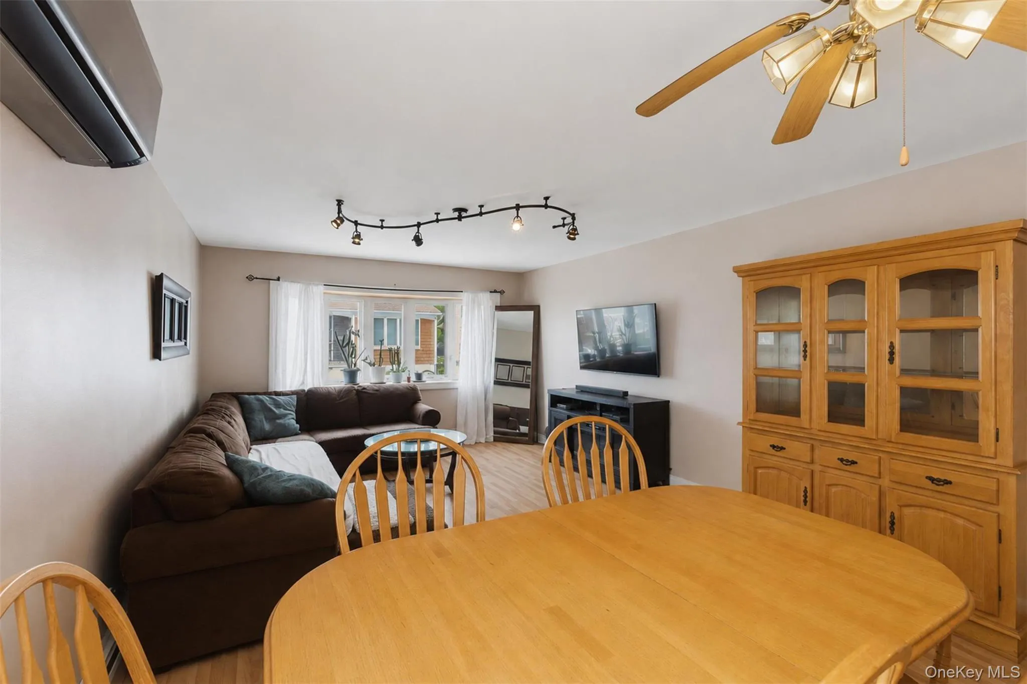 Open-concept living and dining area featuring wood-finish flooring, a bay window with natural light, a ceiling fan, and track lighting Open-concept living and dining area featuring wood-finish flooring, a bay window with natural light, a ceiling fan, and track lighting