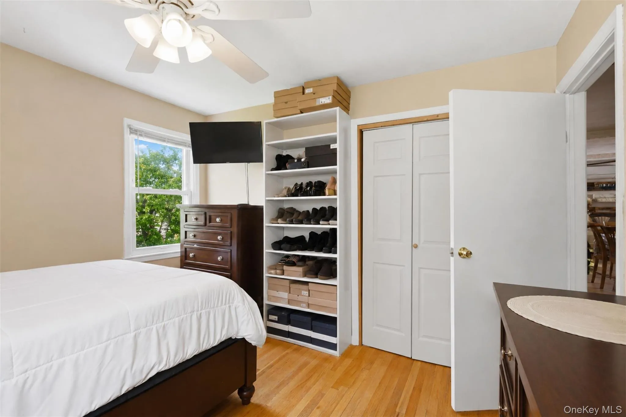 Light-filled room featuring wood-finish flooring, a window with exterior views, a ceiling fan with integrated lighting, and a bi-fold closet Light-filled room featuring wood-finish flooring, a window with exterior views, a ceiling fan with integrated lighting, and a bi-fold closet