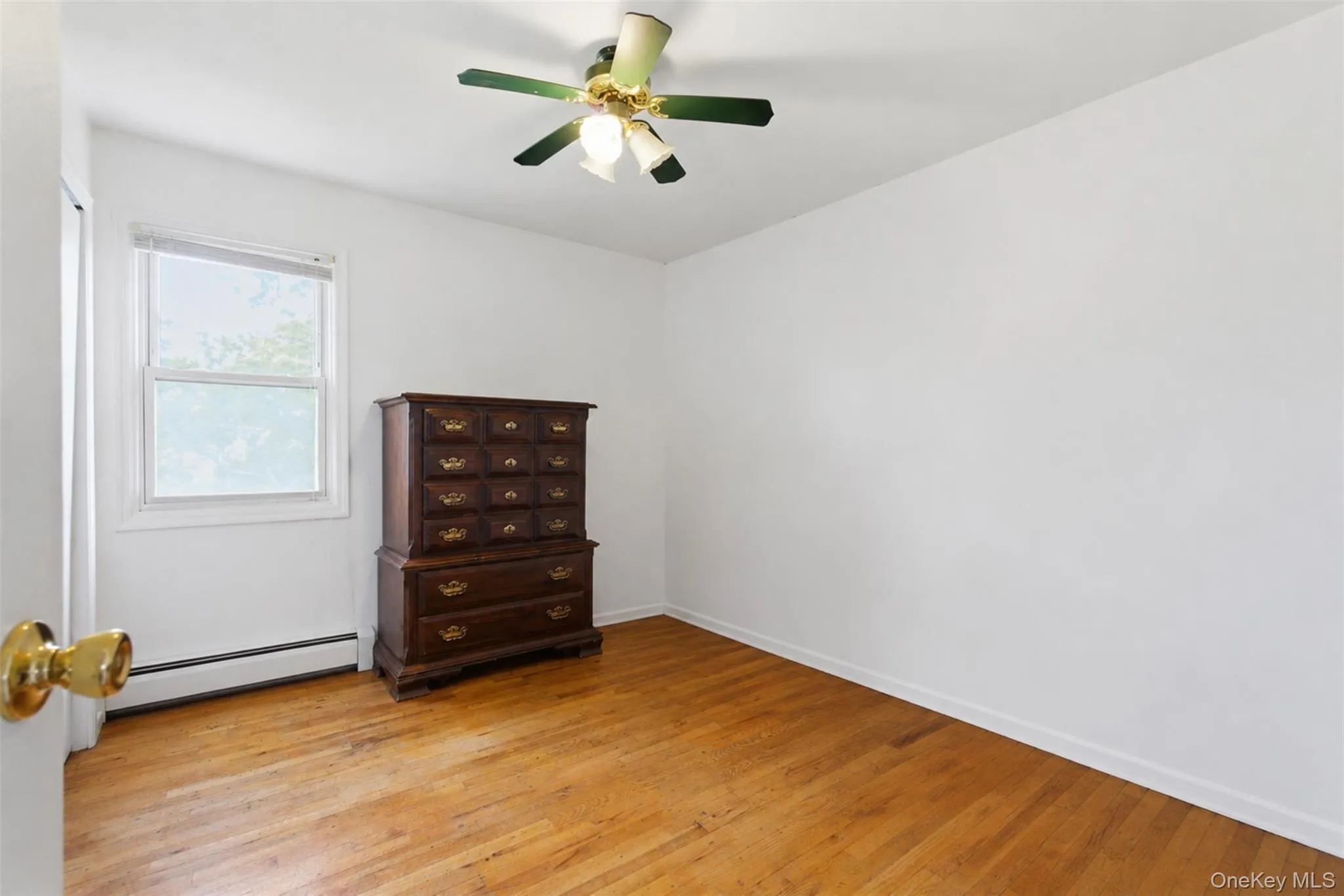 Hardwood flooring throughout featuring white baseboards, a ceiling fan with integrated lighting, and a double-hung window Hardwood flooring throughout featuring white baseboards, a ceiling fan with integrated lighting, and a double-hung window