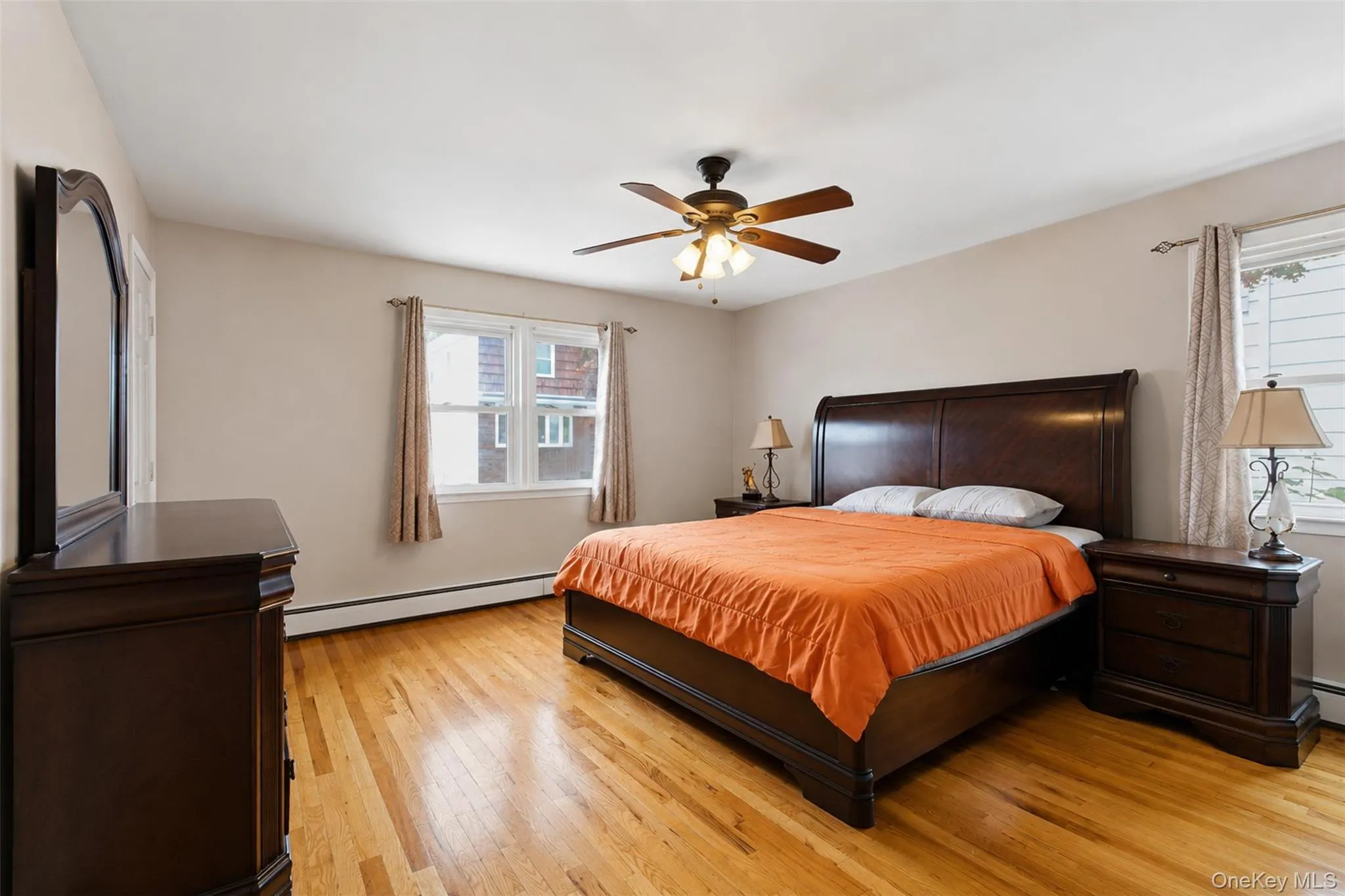 Hardwood flooring features throughout this room with a ceiling fan overhead, two windows, and light-toned walls Hardwood flooring features throughout this room with a ceiling fan overhead, two windows, and light-toned walls