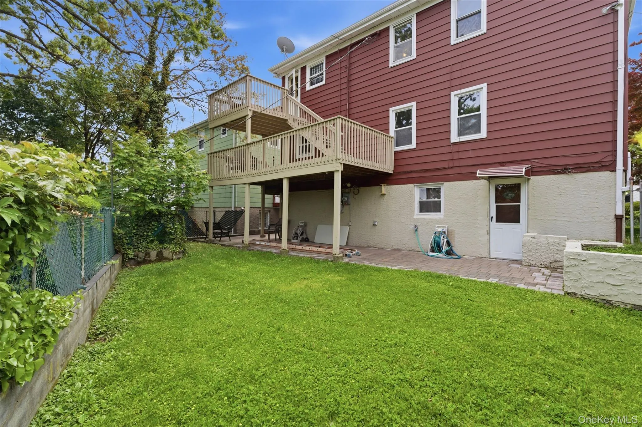 Expansive backyard featuring a manicured lawn, two-story wood deck, chain link fencing, a lower-level patio, and a retaining wall Expansive backyard featuring a manicured lawn, two-story wood deck, chain link fencing, a lower-level patio, and a retaining wall