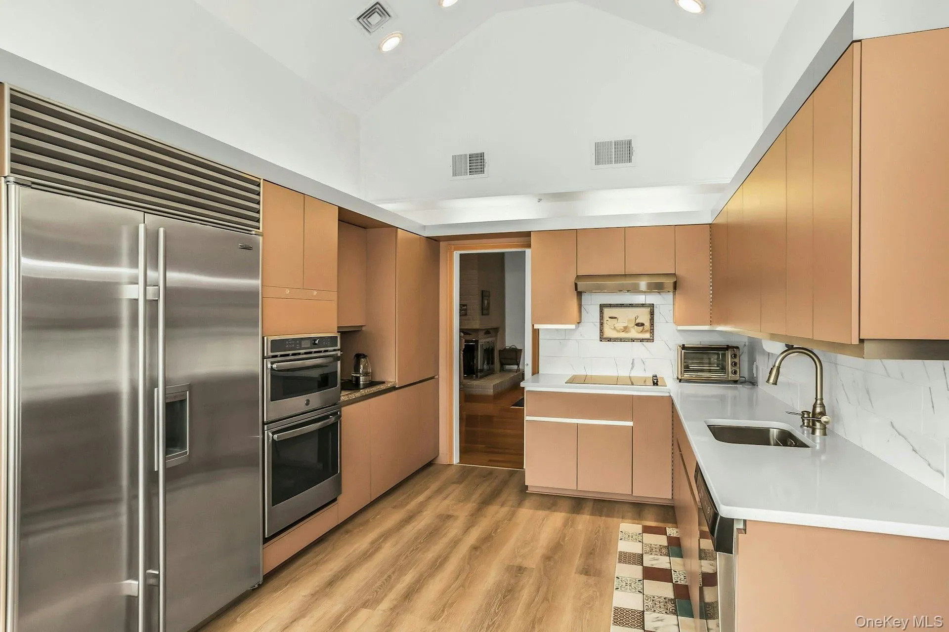 Kitchen with appliances with stainless steel finishes, decorative backsplash, light wood-style flooring, high vaulted ceiling Kitchen with appliances with stainless steel finishes, decorative backsplash, light wood-style flooring, high vaulted ceiling