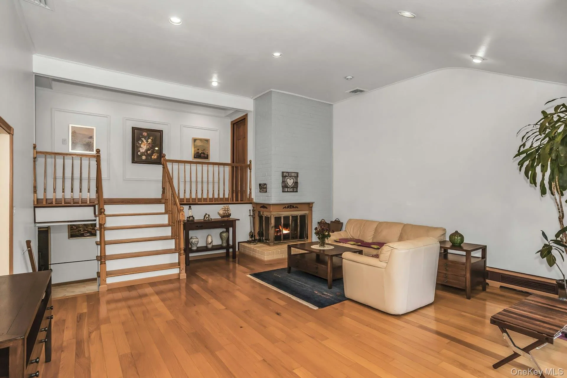 Living area featuring a fireplace, light wood-style floors, vaulted ceiling, stairway, and recessed lighting Living area featuring a fireplace, light wood-style floors, vaulted ceiling, stairway, and recessed lighting
