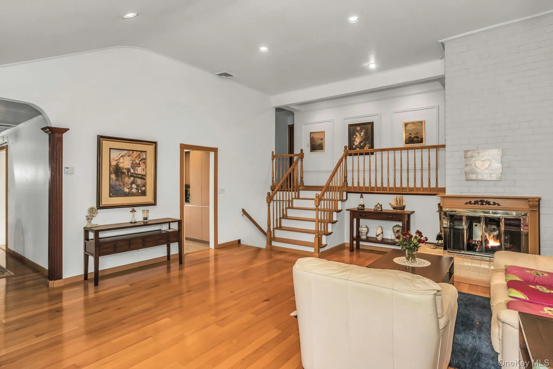 Living room featuring a brick fireplace, stairs, wood finished floors, recessed lighting, and arched walkways Living room featuring a brick fireplace, stairs, wood finished floors, recessed lighting, and arched walkways