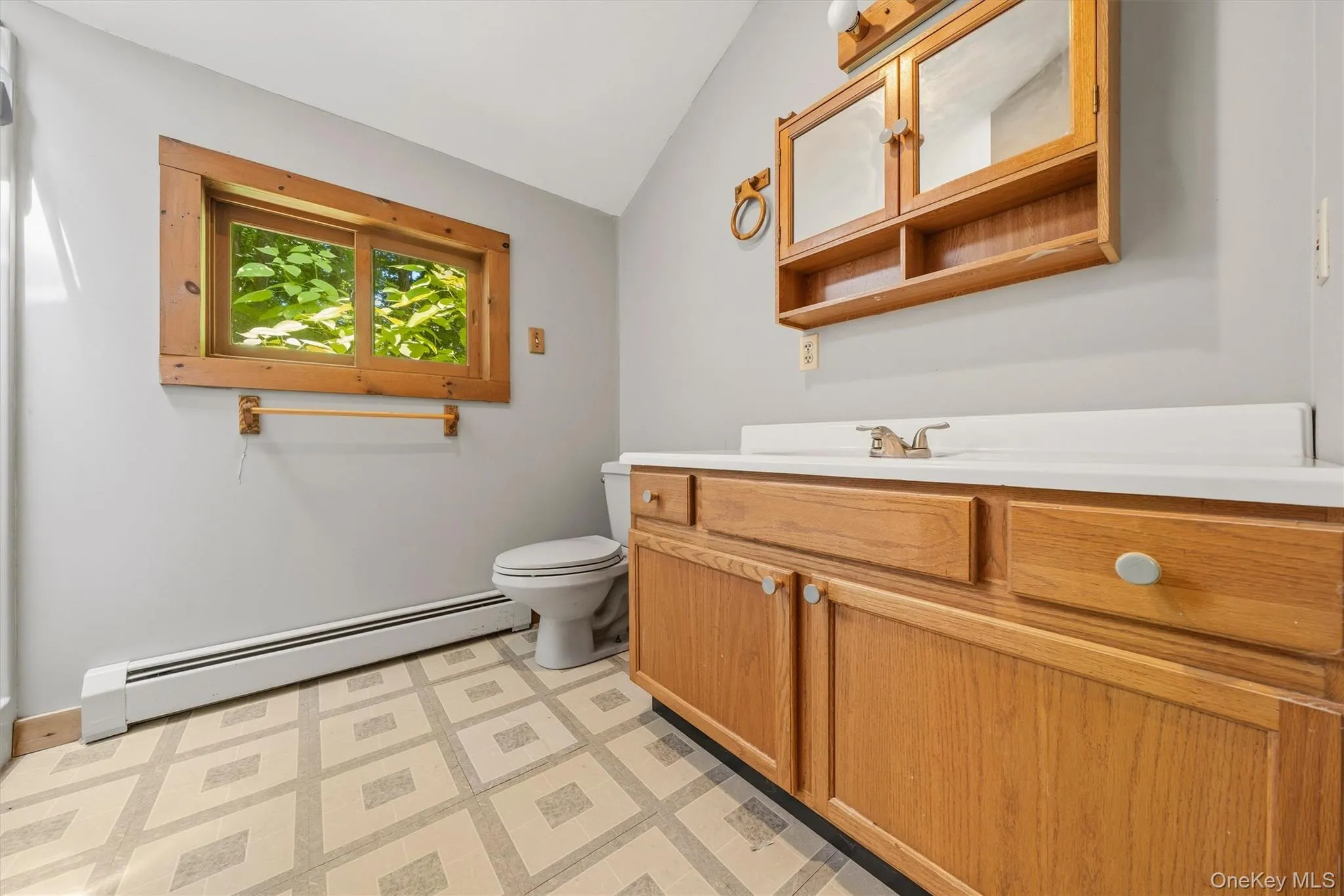 Bathroom featuring a wood-finish vanity with a white countertop and integrated sink, coordinating wood-finish medicine cabinet with mirrored doors, a window with natural wood trim, and geometrically patterned flooring Bathroom featuring a wood-finish vanity with a white countertop and integrated sink, coordinating wood-finish medicine cabinet with mirrored doors, a window with natural wood trim, and geometrically patterned flooring