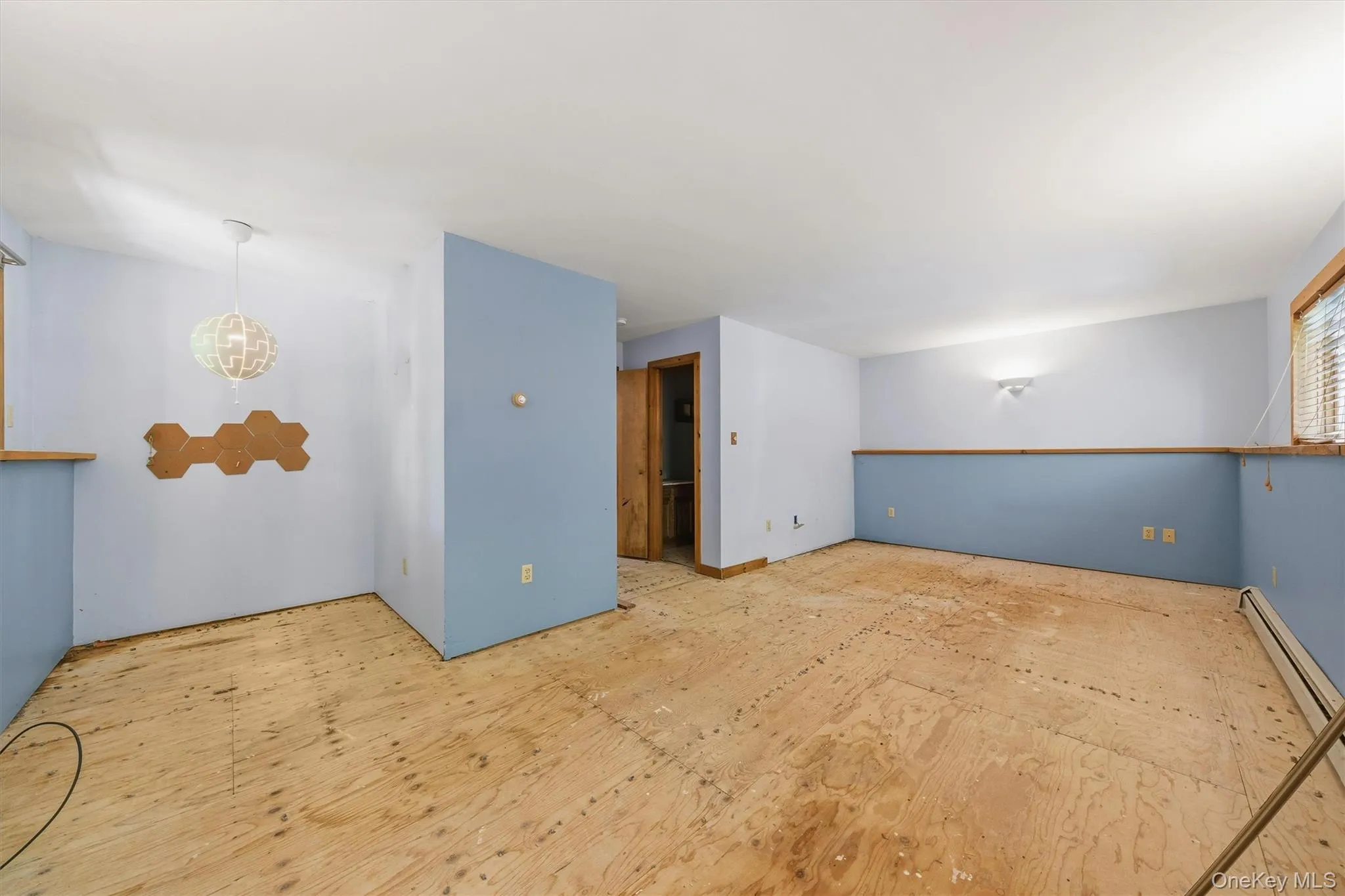 Spacious room featuring light blue and white painted walls with wood trim, exposed subflooring, and a ceiling-mounted light fixture Spacious room featuring light blue and white painted walls with wood trim, exposed subflooring, and a ceiling-mounted light fixture