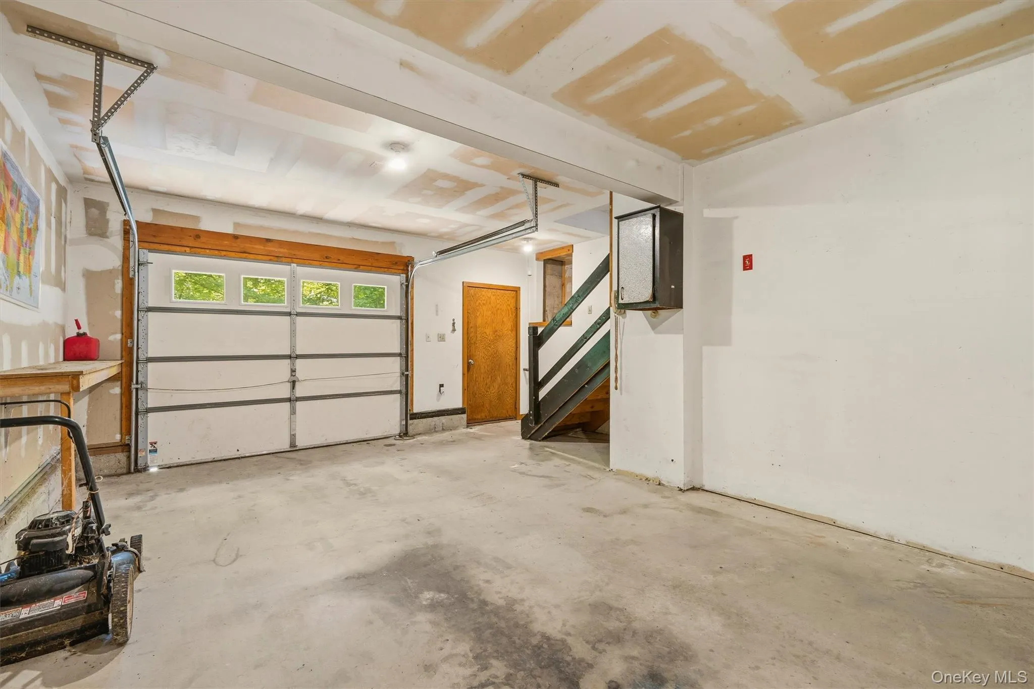 Spacious garage featuring a white overhead door with upper window panels, a concrete floor, and an exposed ceiling Spacious garage featuring a white overhead door with upper window panels, a concrete floor, and an exposed ceiling