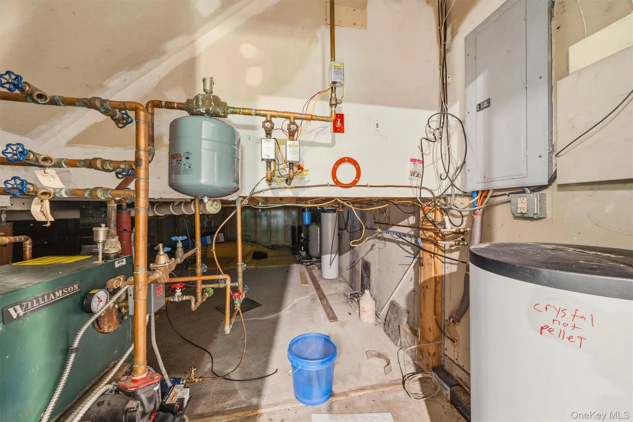 Utility area featuring a Williamson boiler, extensive copper piping, a pressure tank, a large water heater, and an electrical service panel Utility area featuring a Williamson boiler, extensive copper piping, a pressure tank, a large water heater, and an electrical service panel